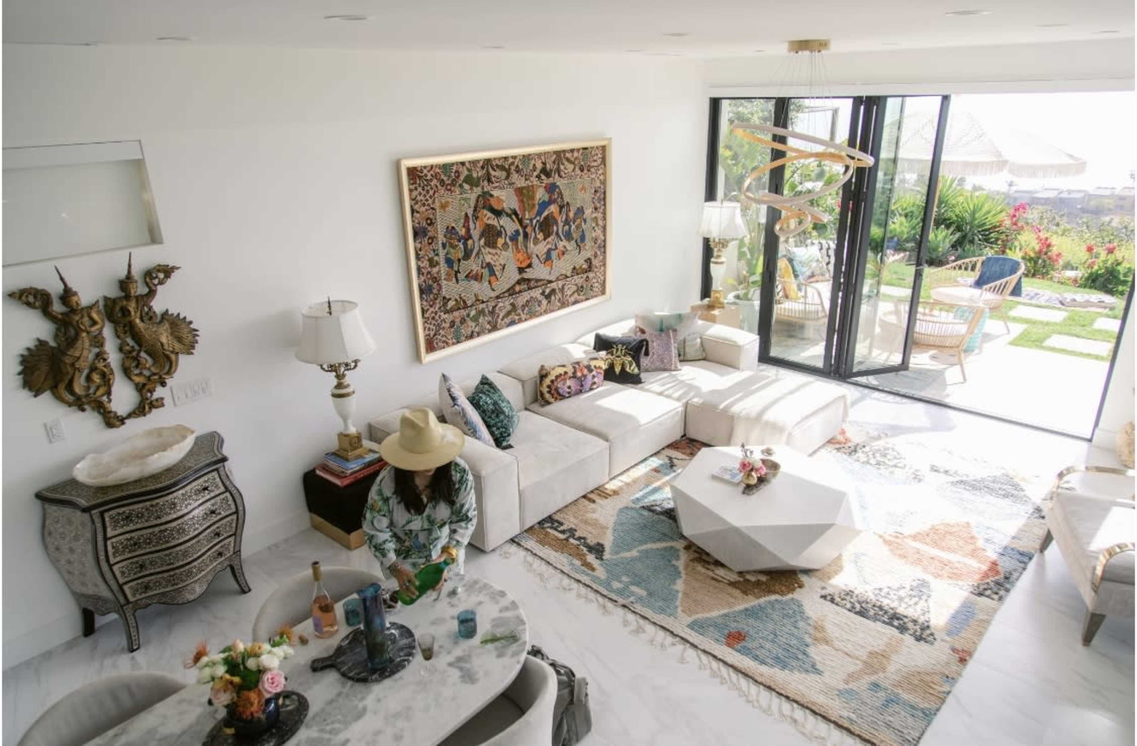 A bright living room features a white sectional sofa, a patterned rug, a coffee table, and large glass doors leading to an outdoor patio.