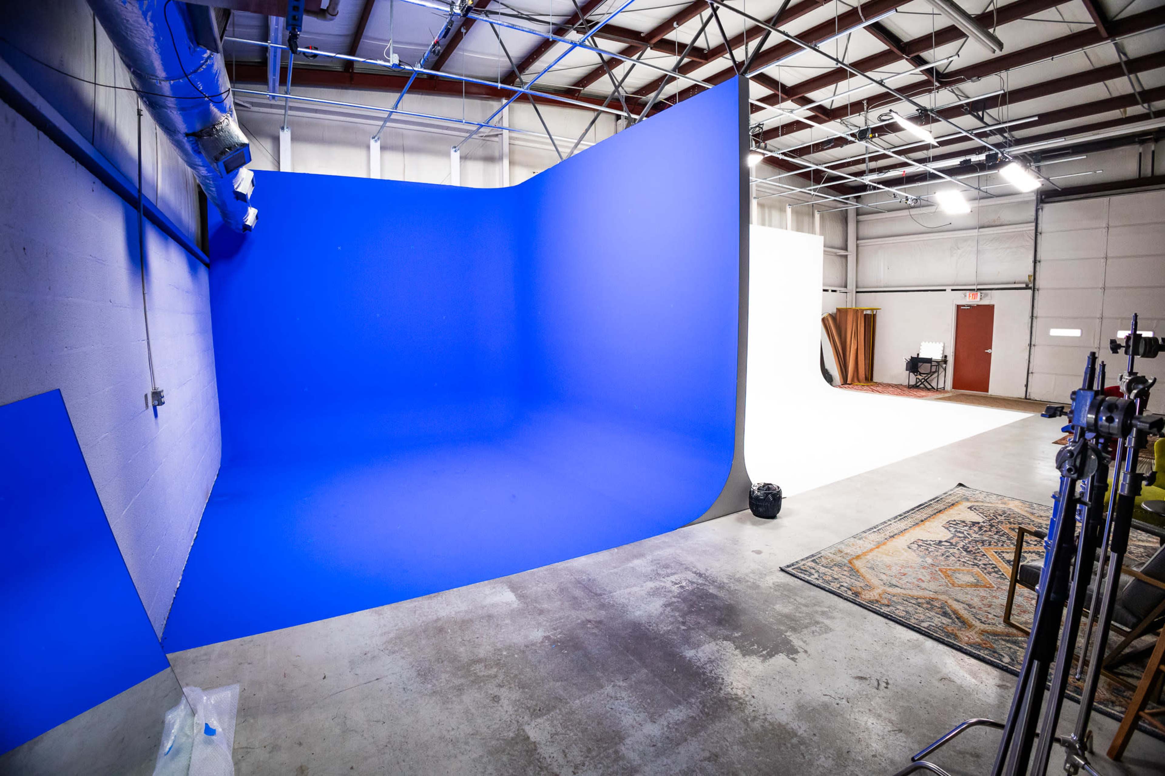 The image shows a studio space featuring a large blue backdrop on one side and a white backdrop on the opposite side, with various equipment and a rug on the floor.