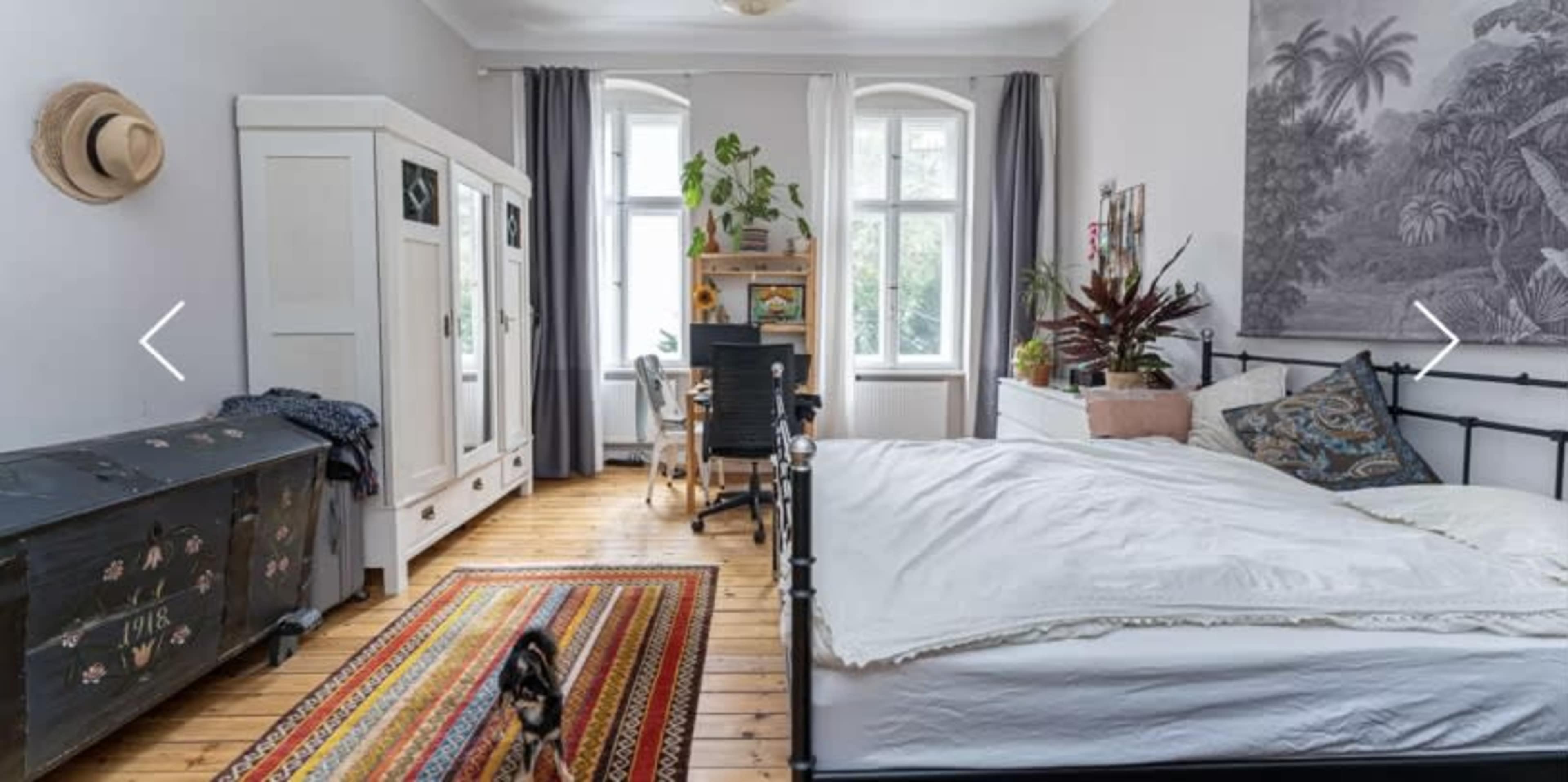 A well-furnished bedroom featuring a bed, a desk with a chair, a wardrobe, and a colorful rug on wooden flooring.