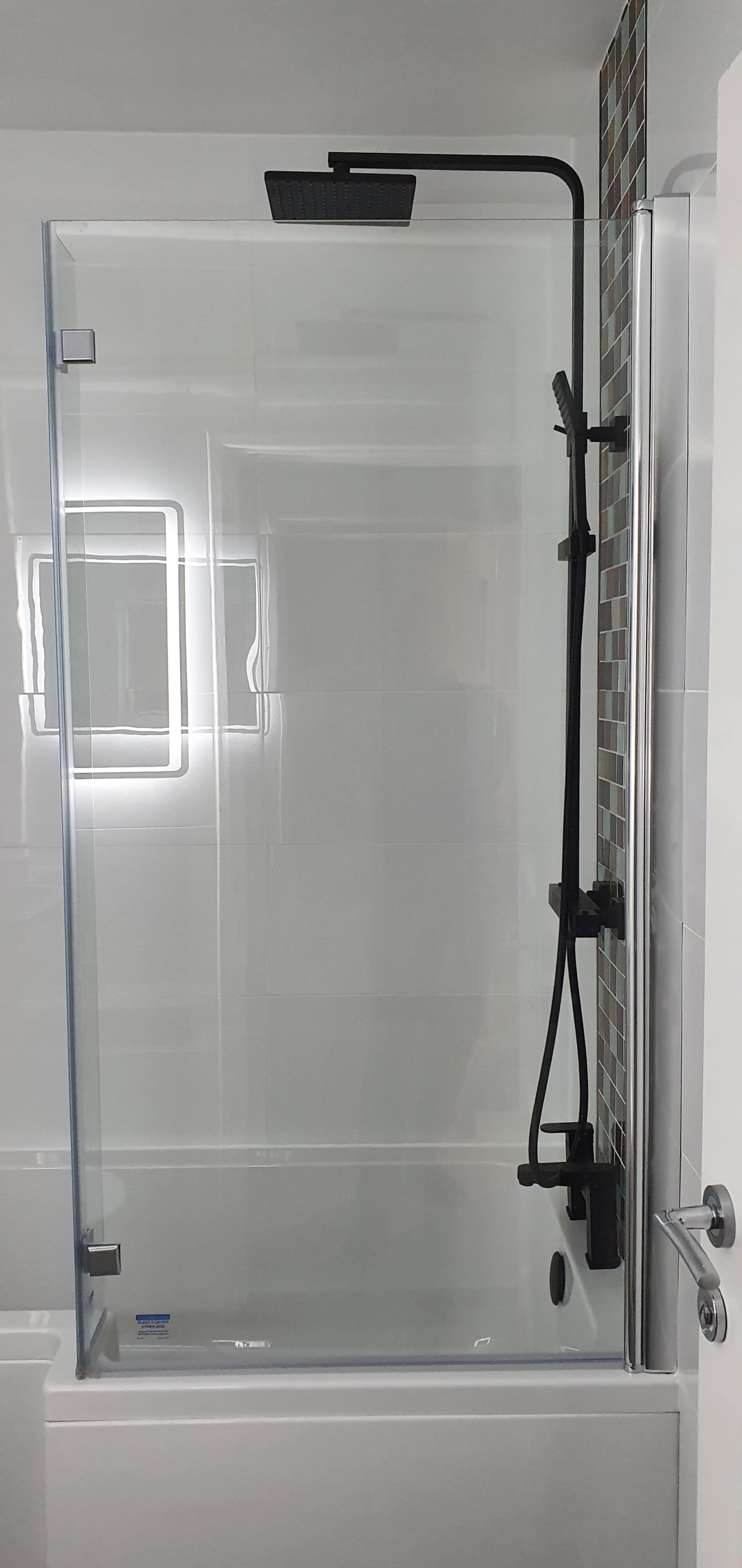 A modern shower enclosure with a glass door, a fixed showerhead, and a handheld shower attachment on a tiled wall.
