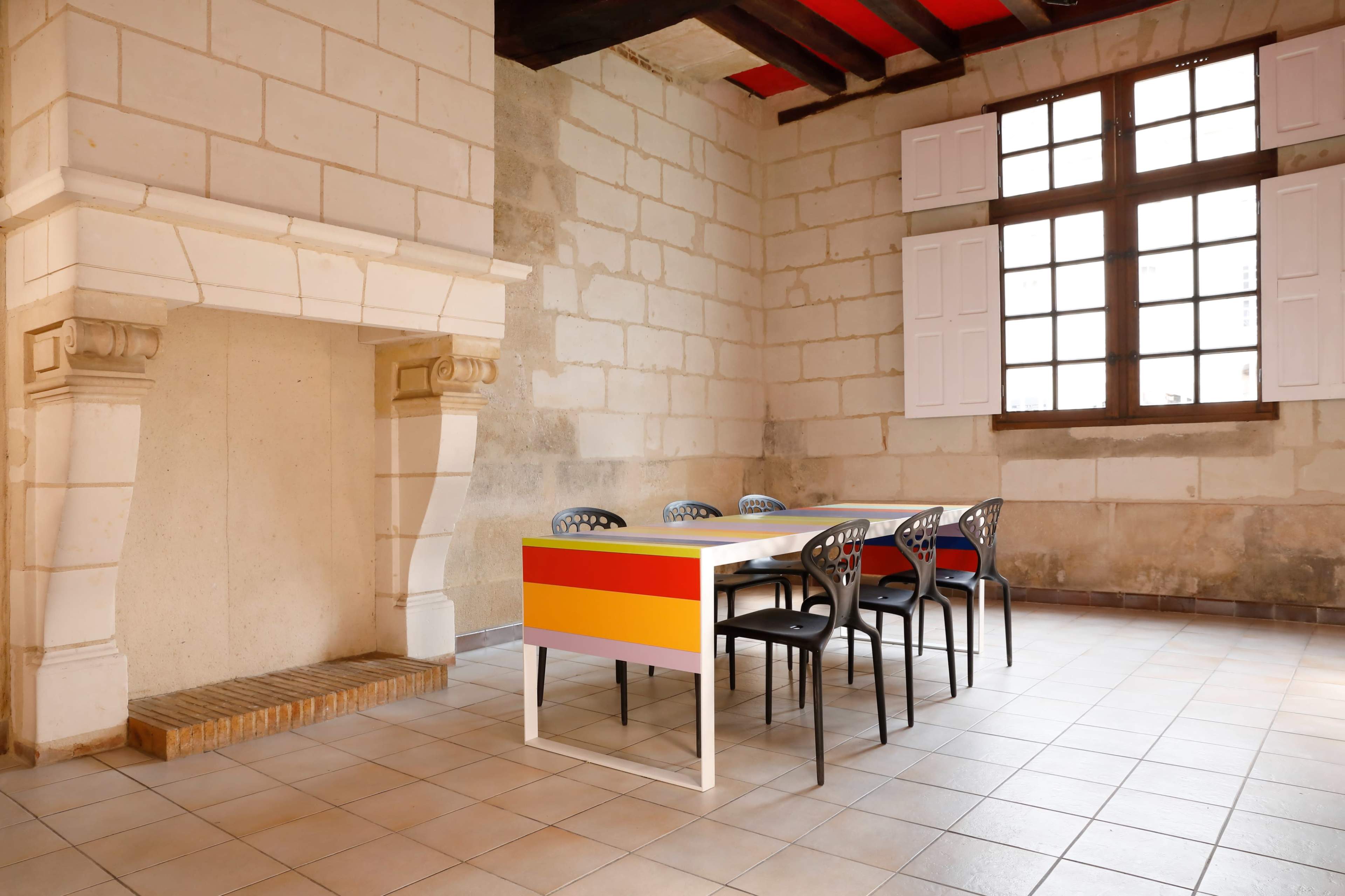 The image shows a spacious room with stone walls, featuring a wooden table surrounded by six black chairs and a large fireplace.