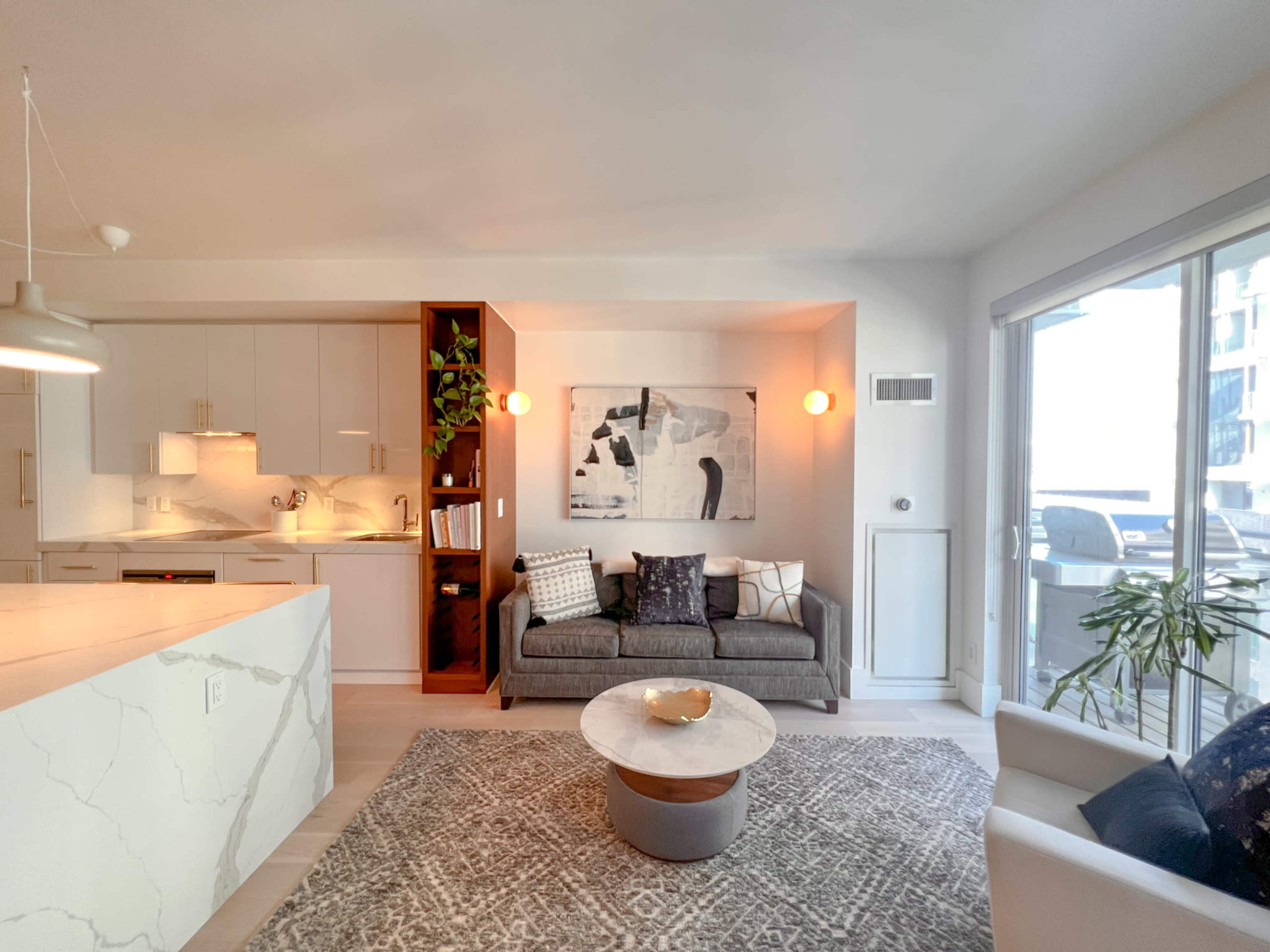 A modern living room with a gray sofa, a round coffee table, and an open kitchen area with a marble countertop.