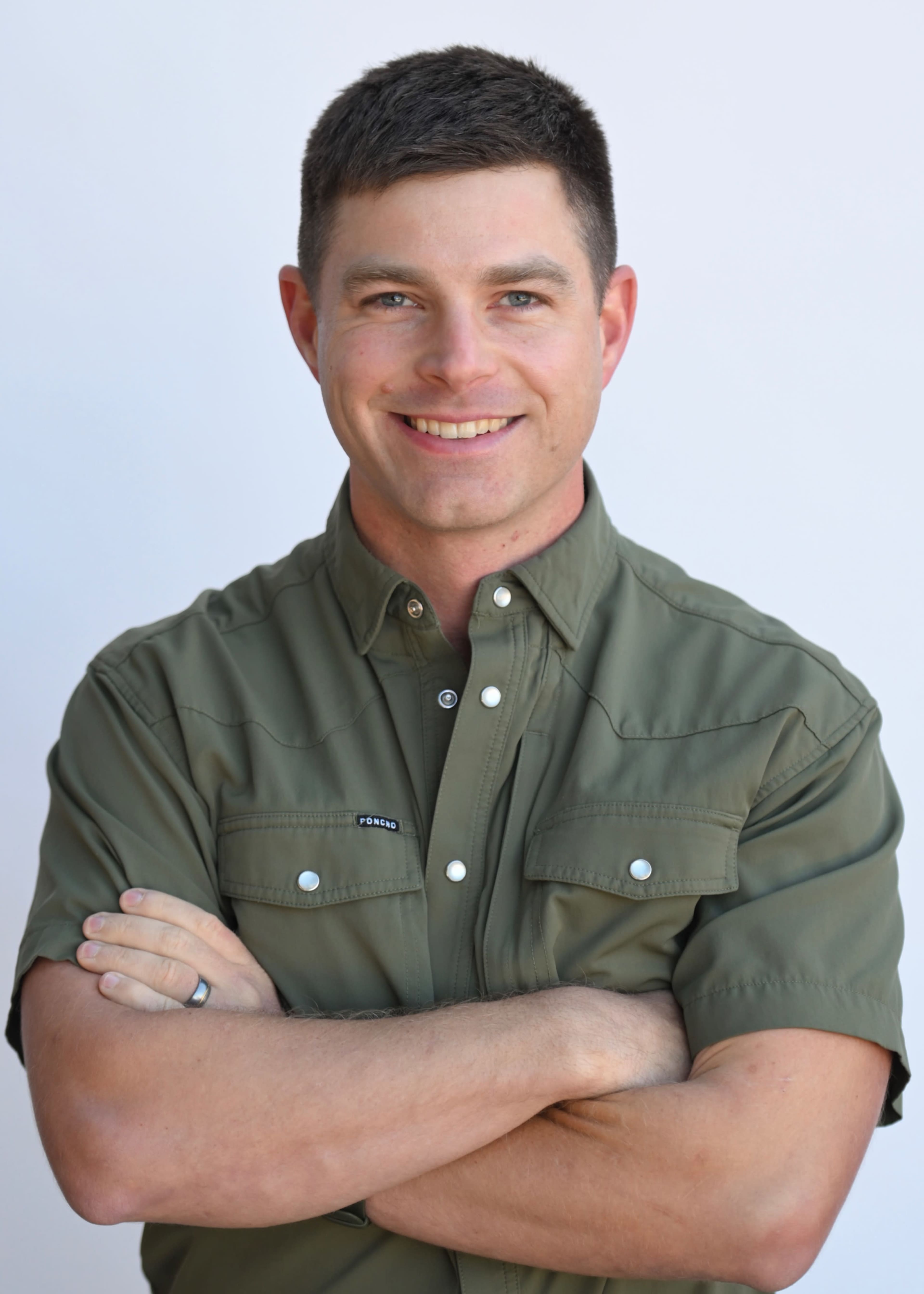 A man with short hair wearing a green button-up shirt stands with his arms crossed, smiling at the camera.