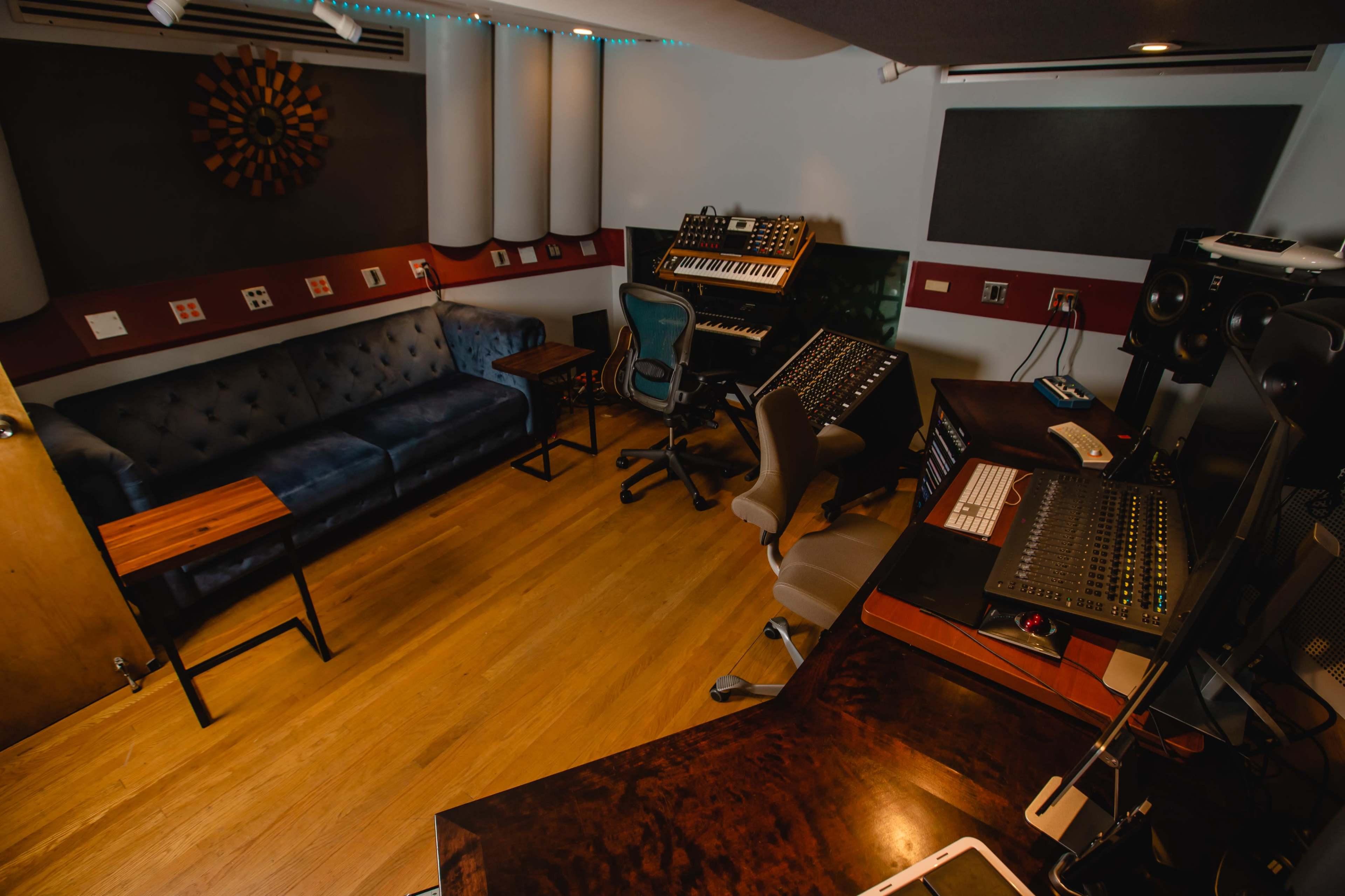 A recording studio with a couch, various music equipment, and workstations arranged around the room.