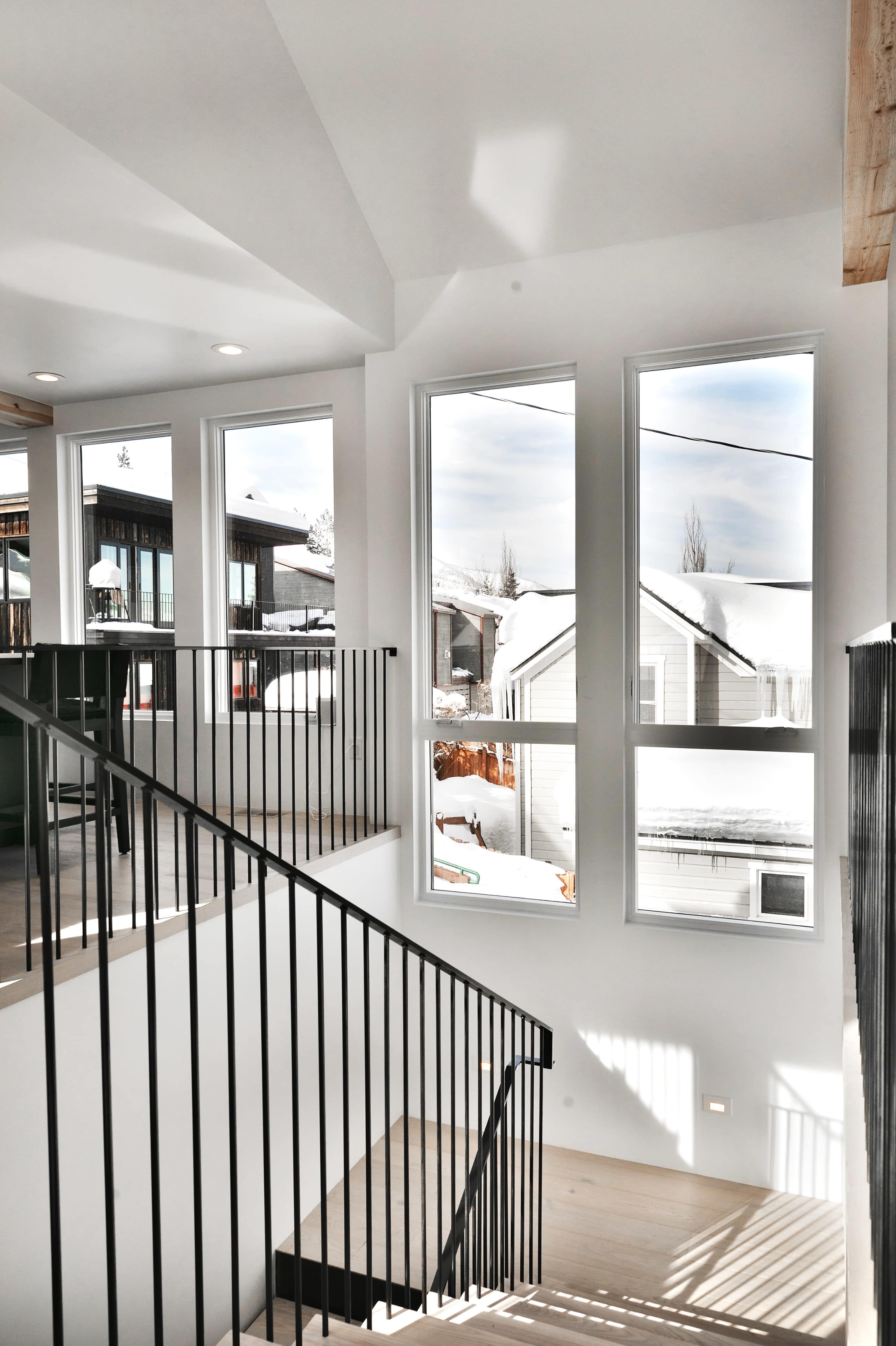 A staircase with black metal railings and large windows that overlook a snowy landscape.