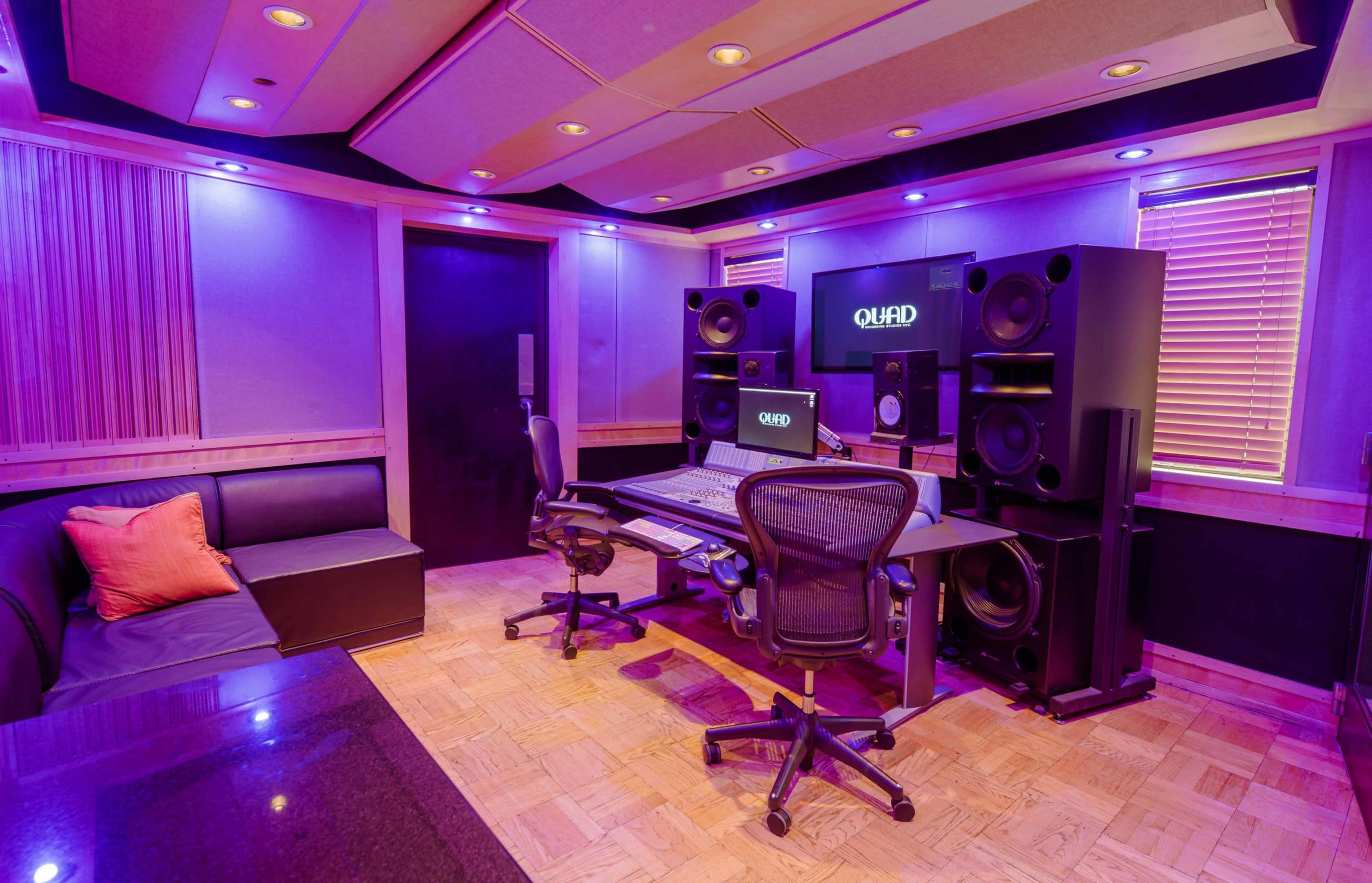 A modern recording studio features a central mixing desk surrounded by large speakers, ambient lighting, and a comfortable seating area.