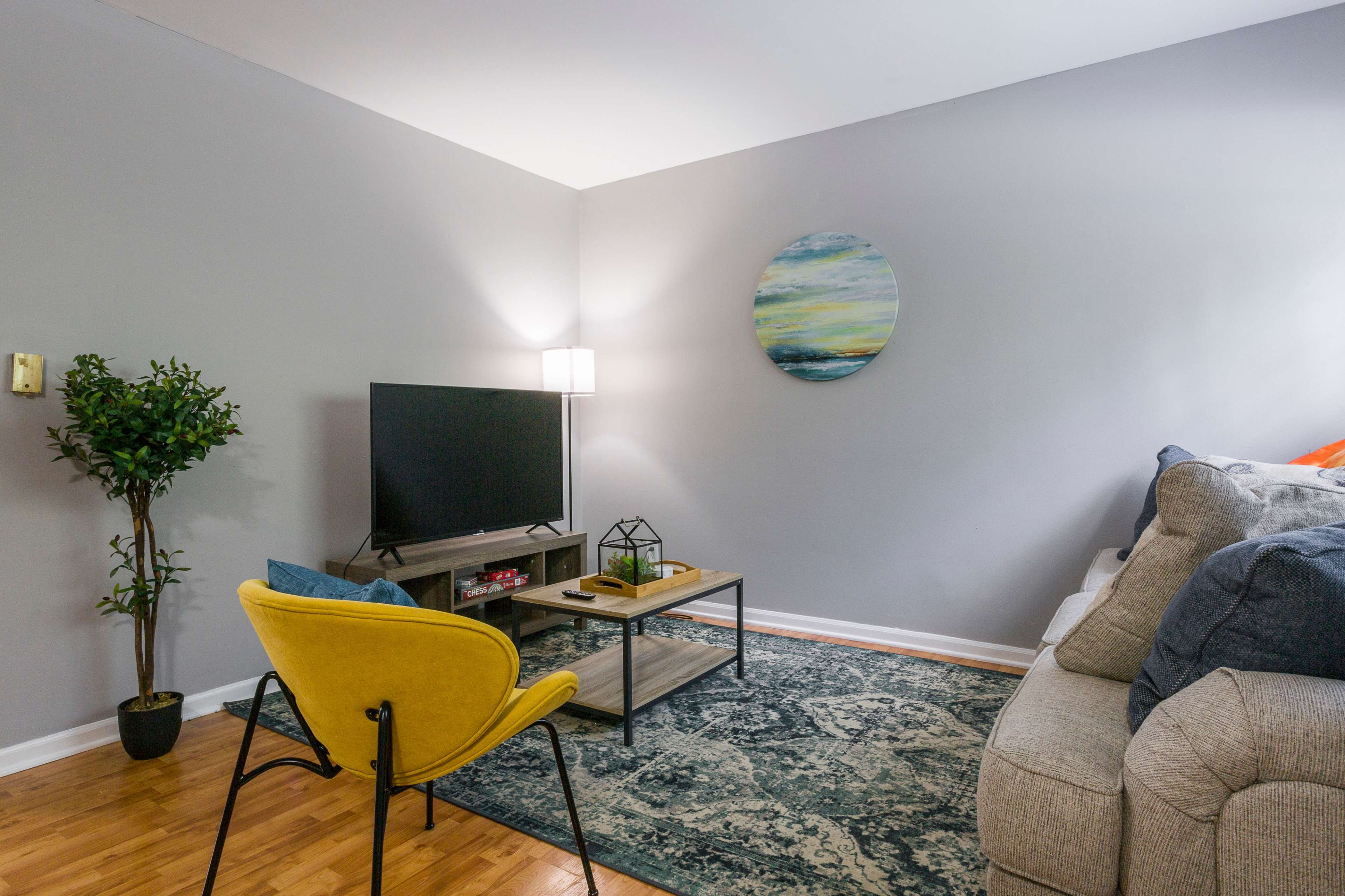 A living room featuring a gray wall, a television on a stand, a yellow chair, a coffee table, and a potted plant.