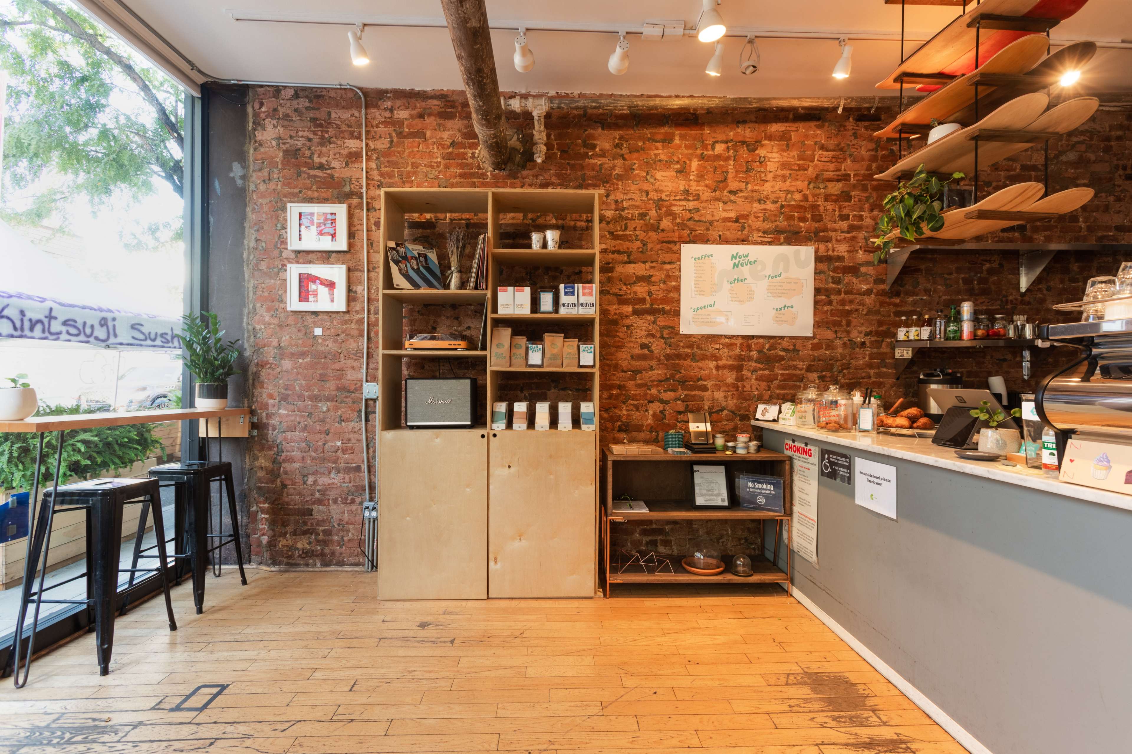 A cozy café interior featuring brick walls, wooden shelves with various items, and a counter with a coffee machine.
