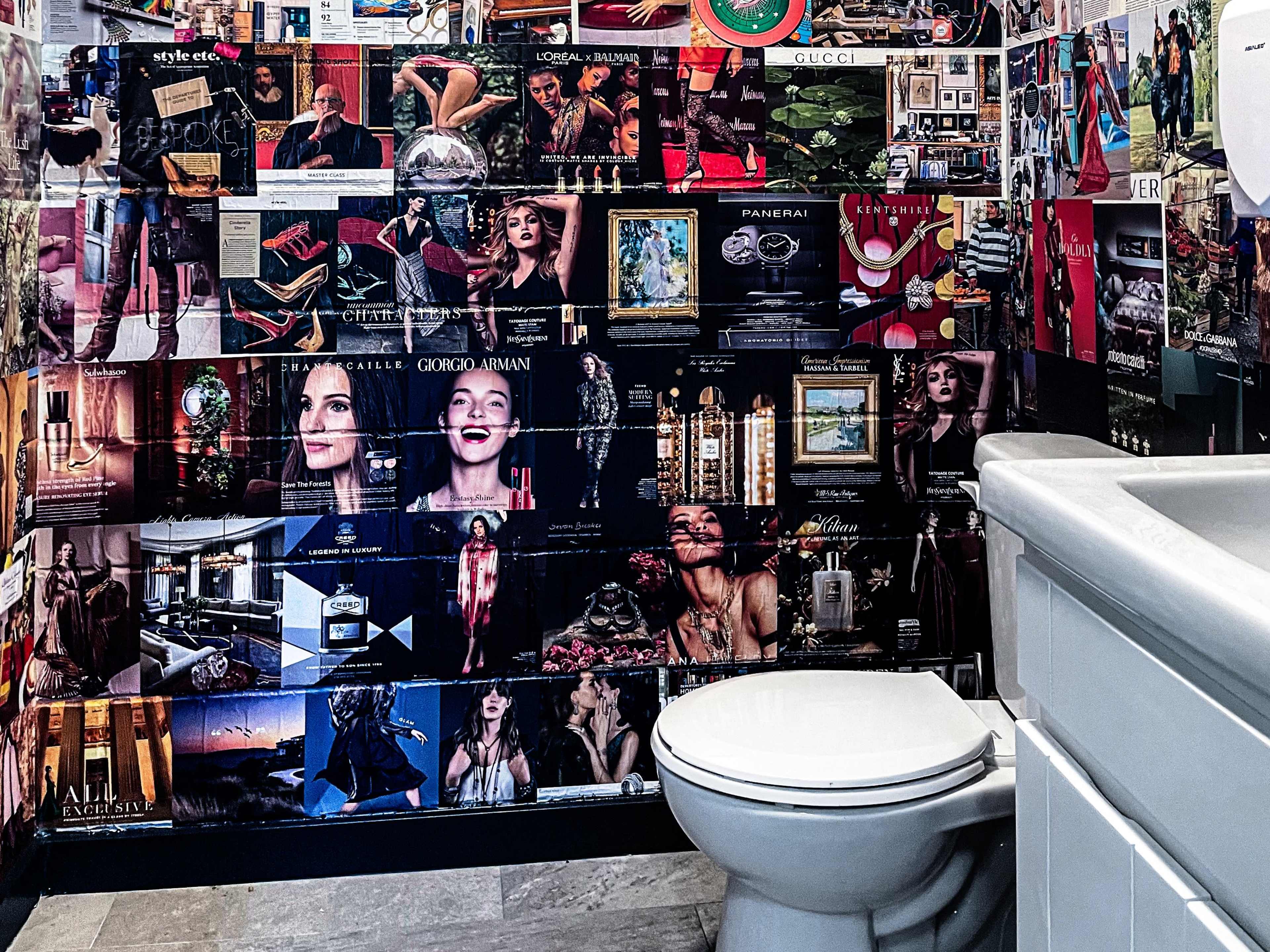 A bathroom with a collage of fashion and beauty advertisements covering the walls, alongside a white toilet and sink.