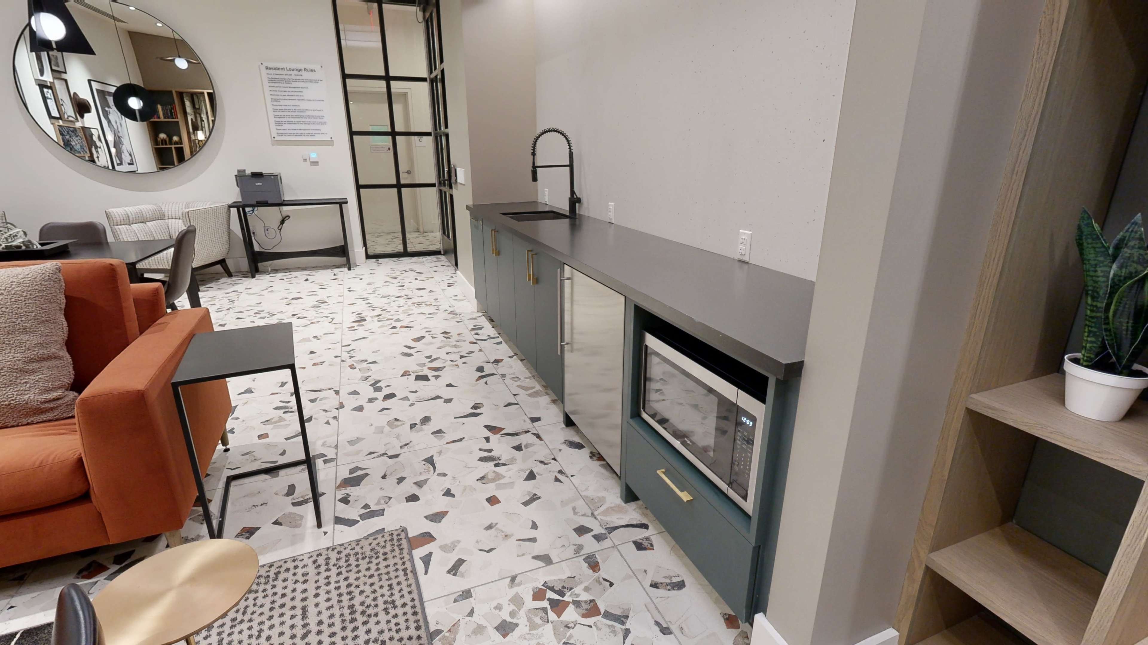 A modern kitchen space with a long countertop, a sink, and a built-in refrigerator, set against a backdrop of terrazzo flooring and minimalist furnishings.