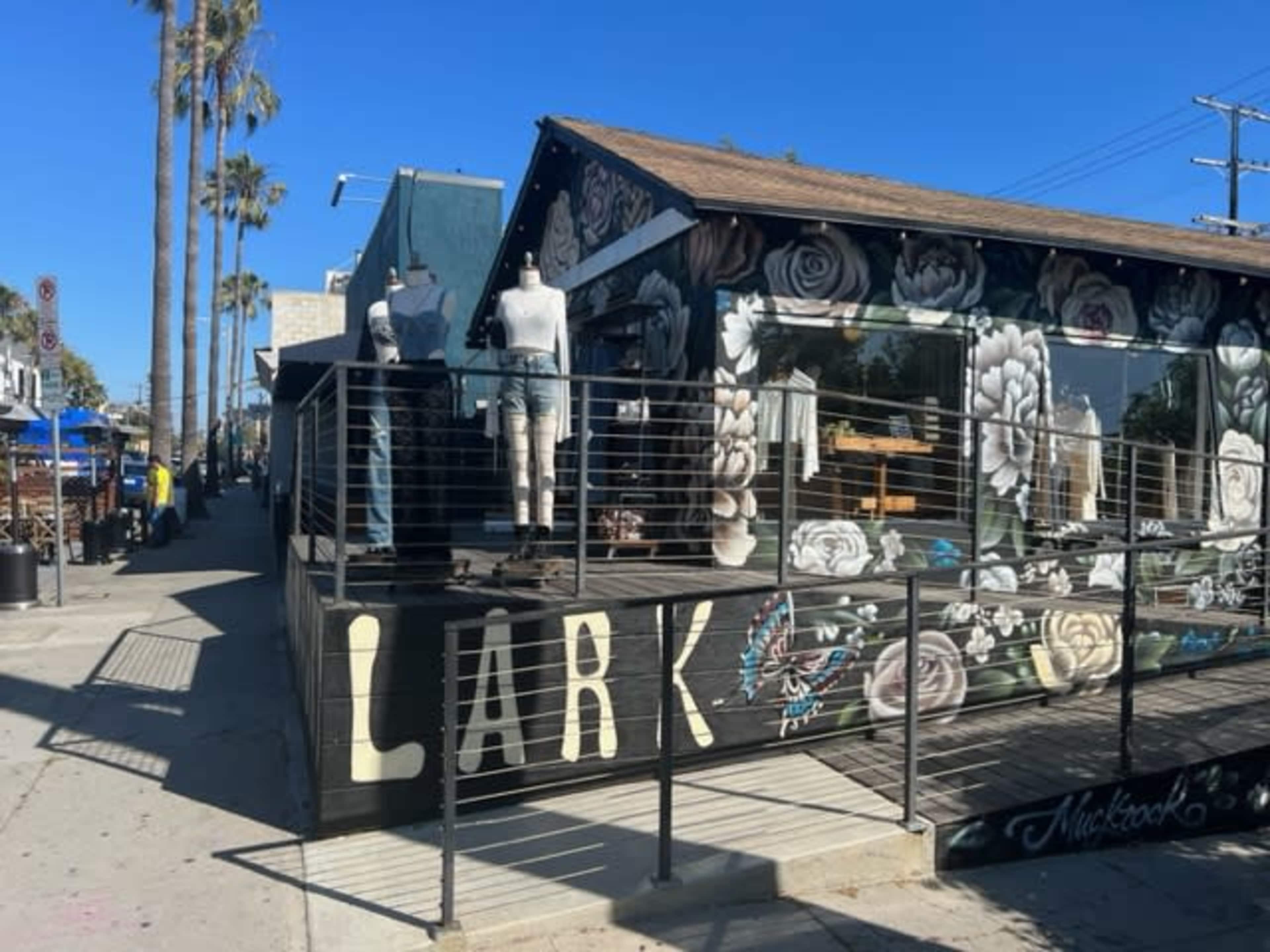 The image shows a retail store called "Lark," featuring a decorated exterior with large floral murals and mannequins displayed on the porch.
