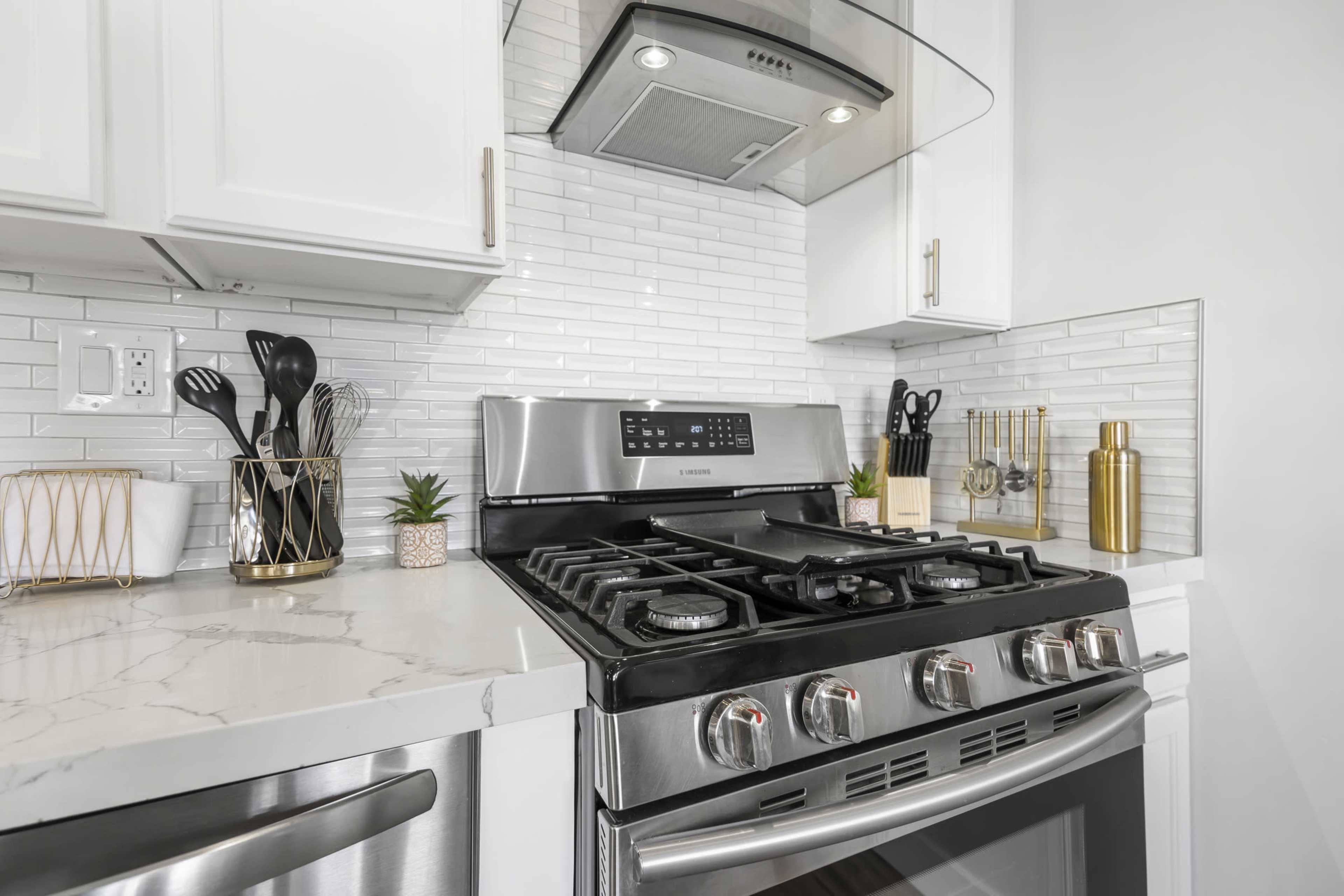 A modern kitchen countertop featuring a stainless steel gas range, a sleek hood, and organized cooking utensils in a stylish holder.