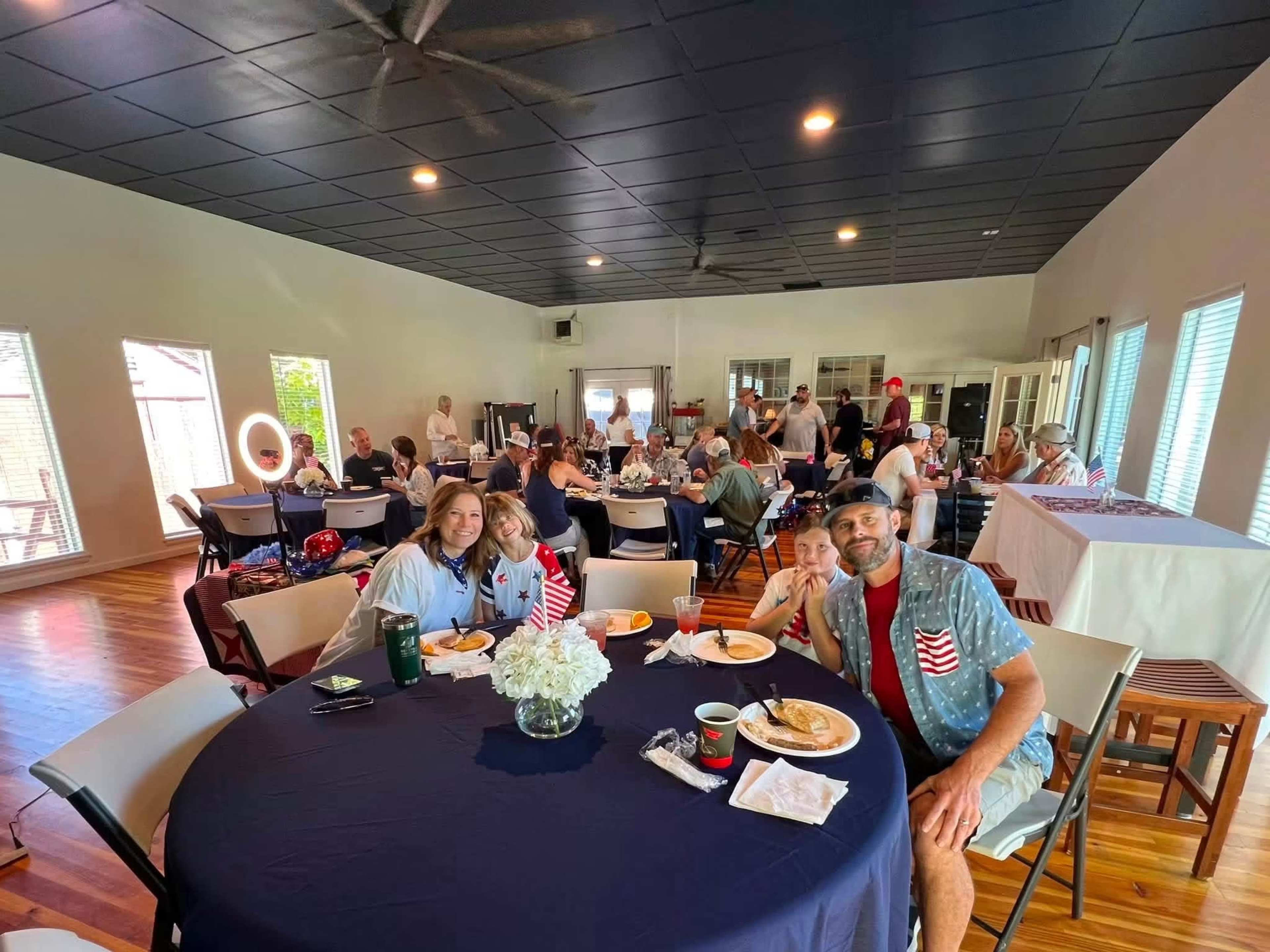 A group of people are seated at tables in a community hall, enjoying a meal together.