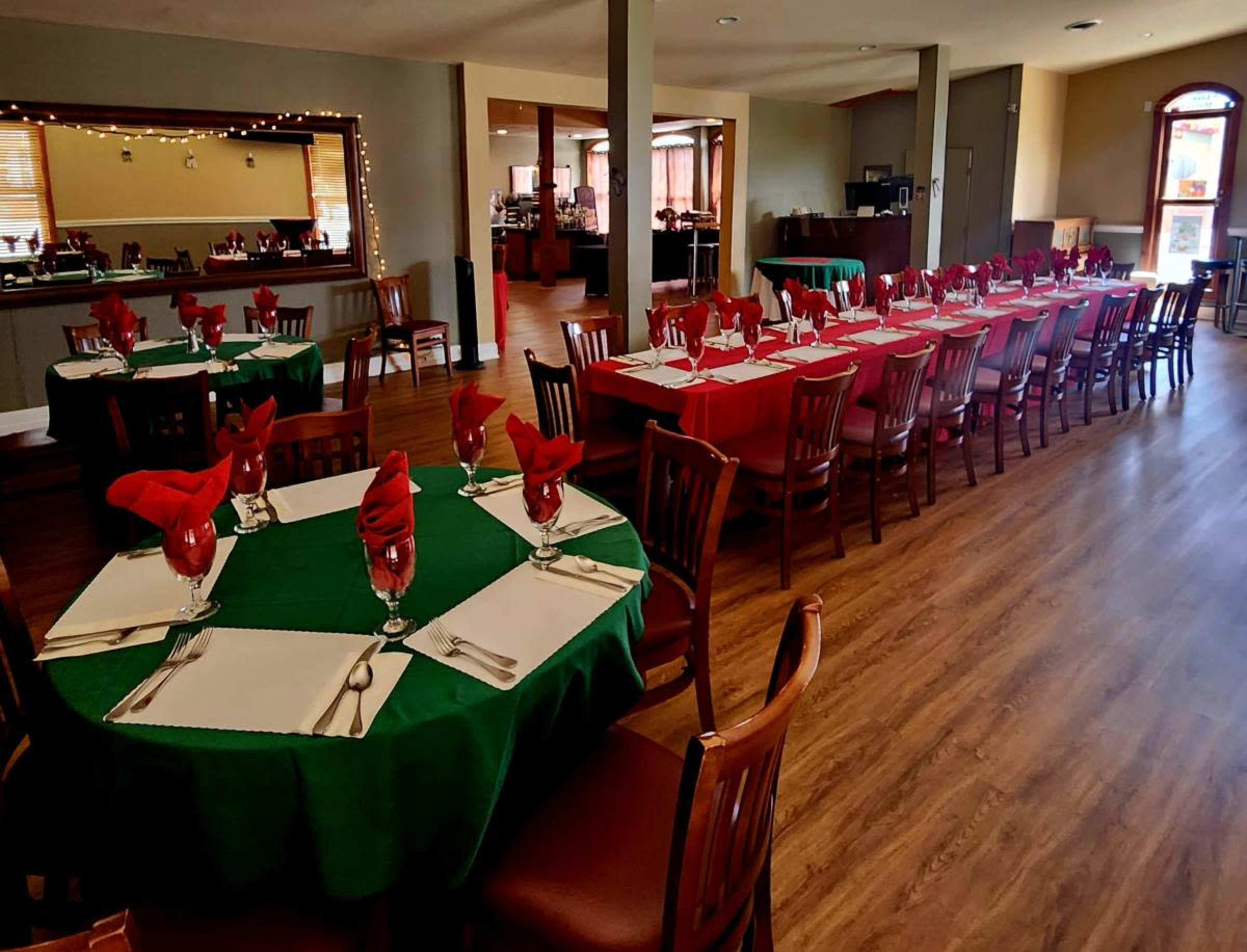 A dining area set for an event, featuring multiple tables decorated with green and red tablecloths and napkins.