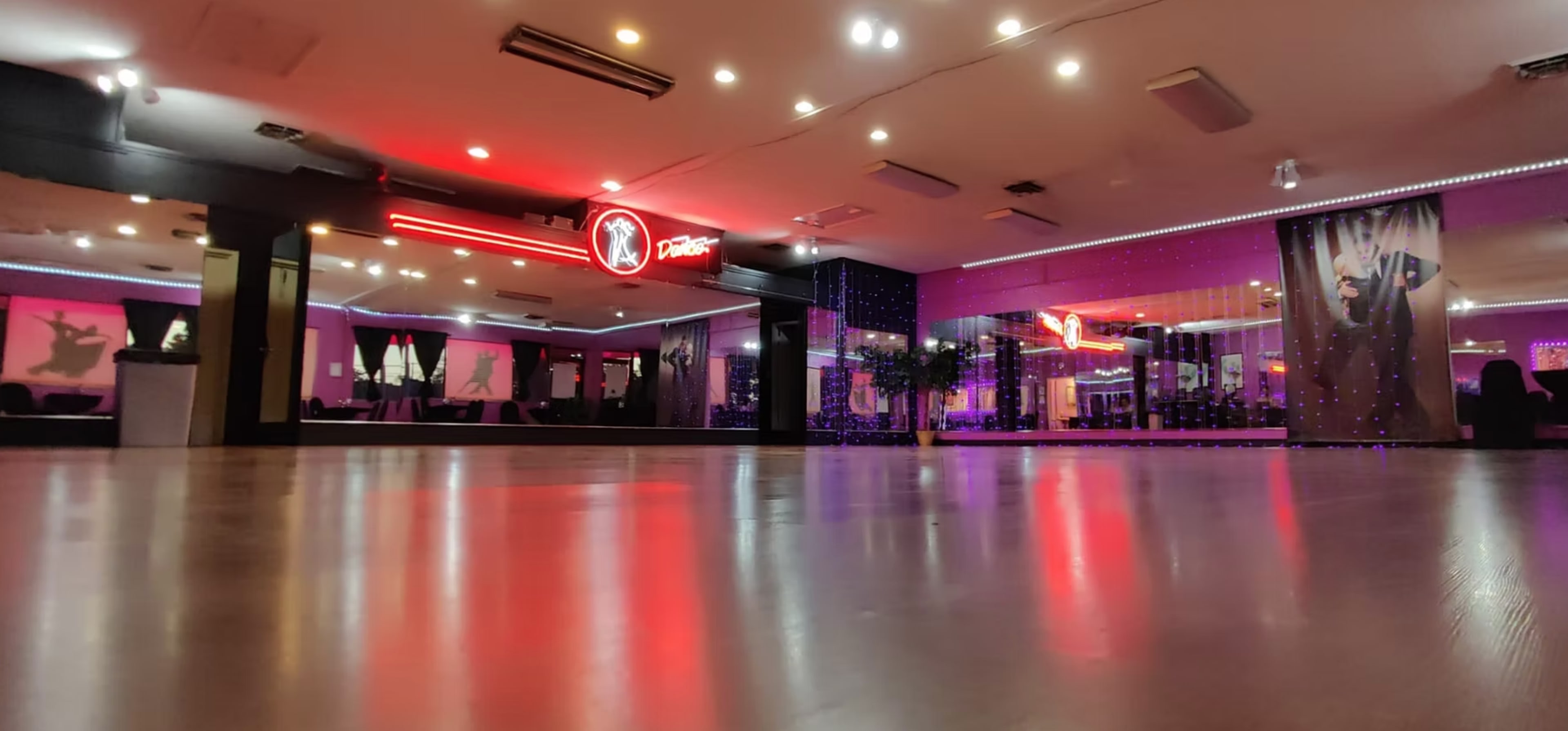 The image shows a modern dance studio with vibrant lighting, including red accents, and a polished wooden floor.