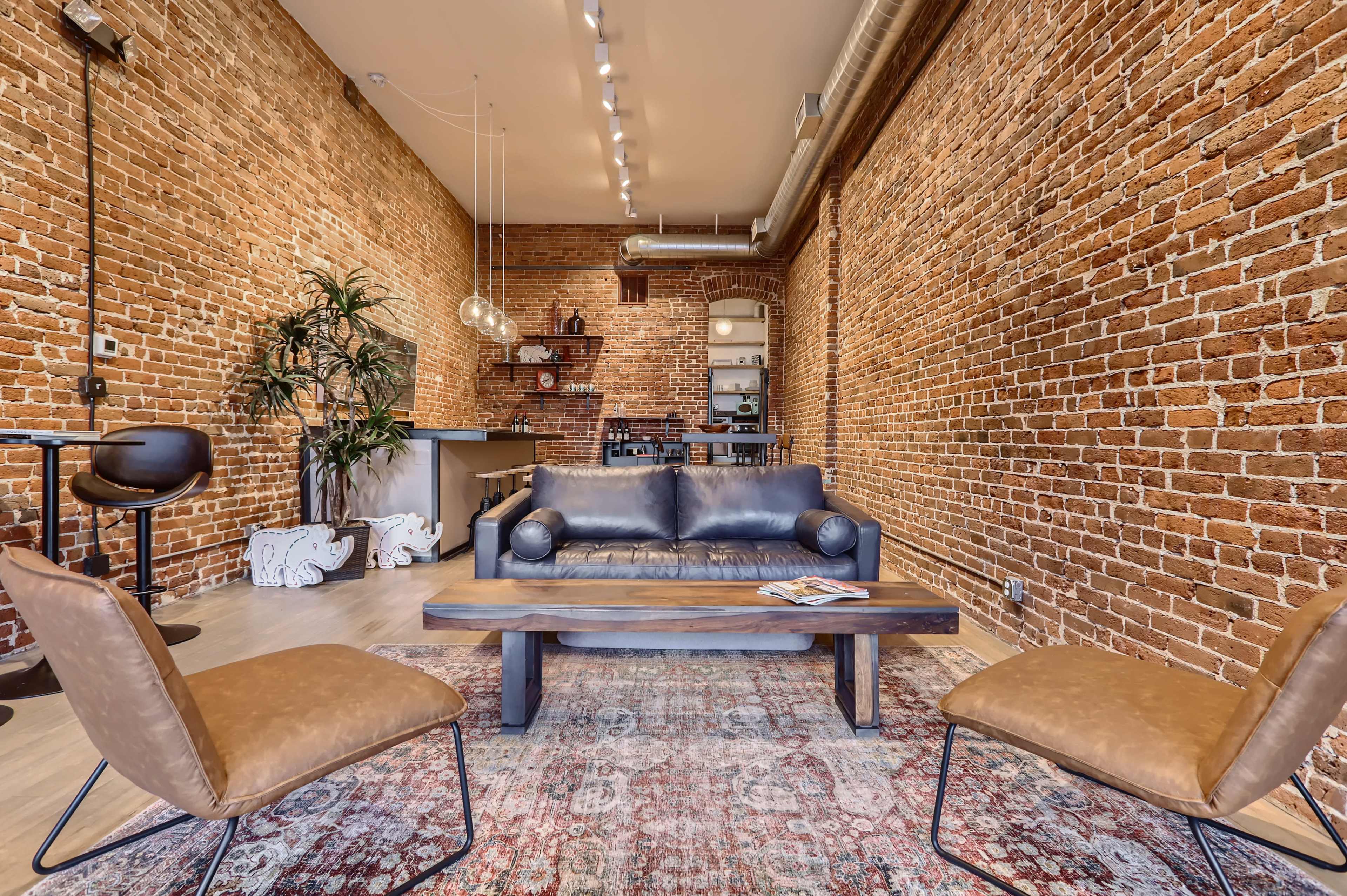 A modern interior featuring a leather sofa, two chairs, and exposed brick walls in a spacious living area.