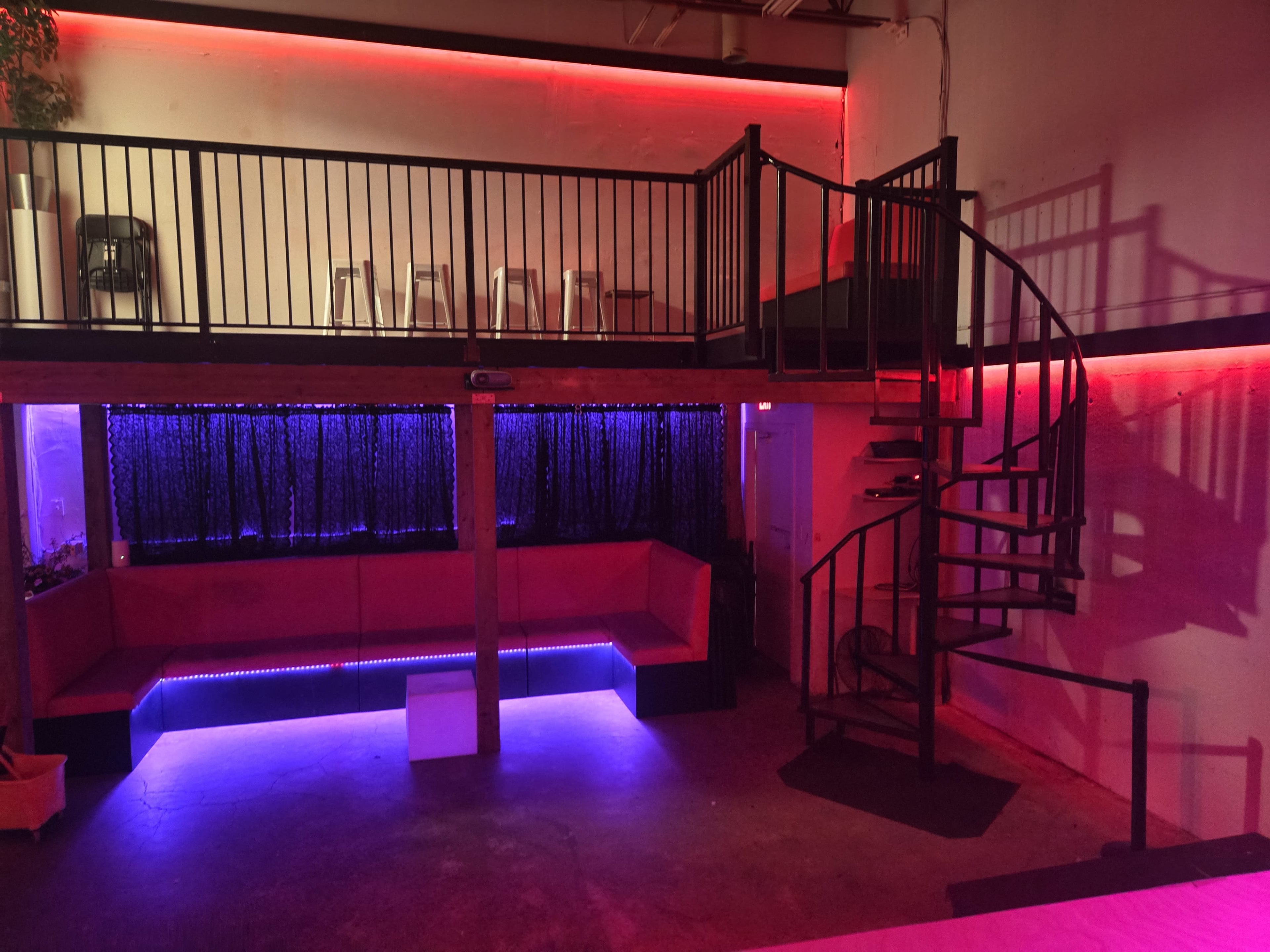 The image shows a modern interior space with a spiral staircase, a raised seating area, and ambient lighting in red and purple tones.