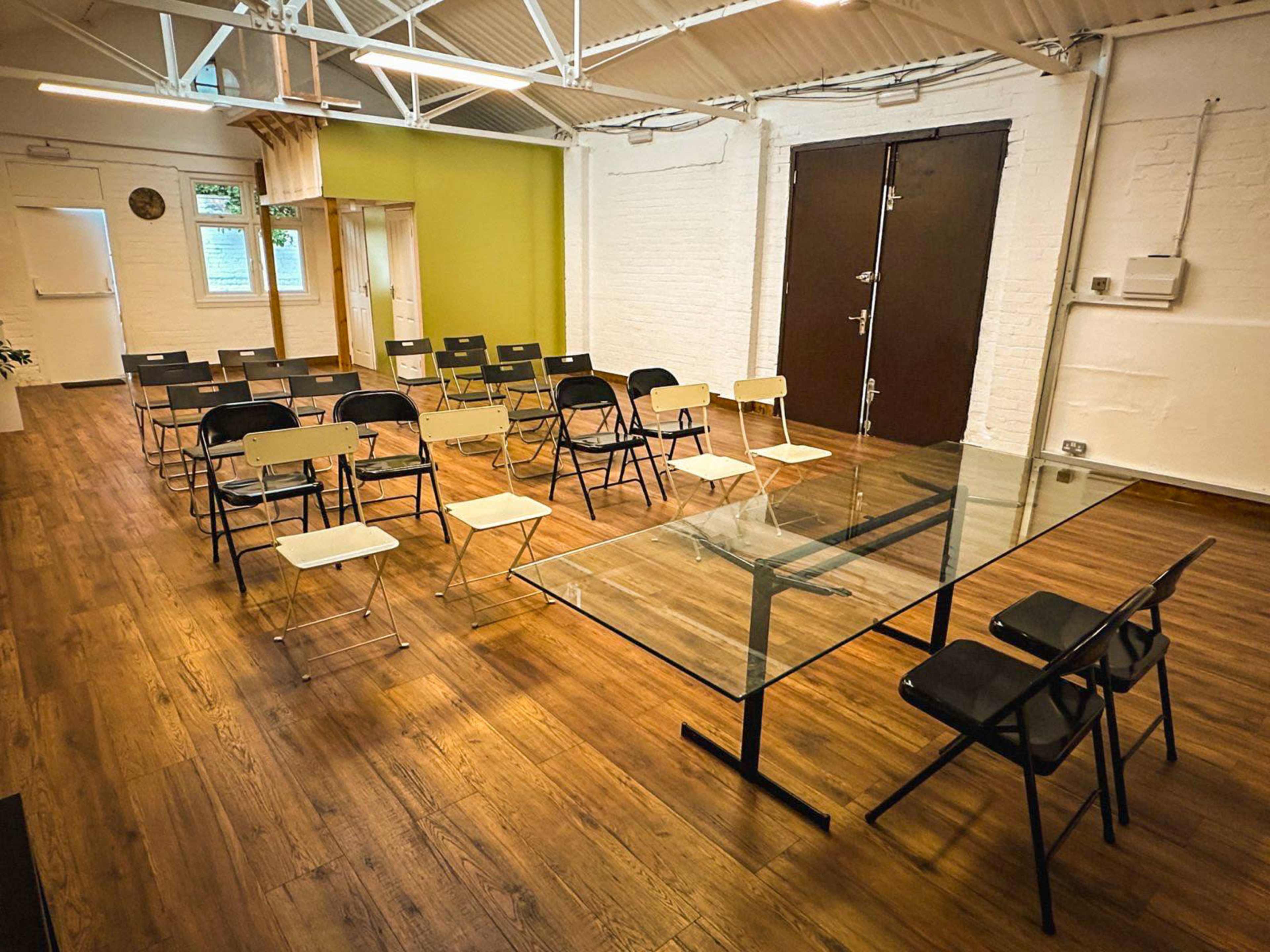 A modern meeting room features a glass table surrounded by black and white chairs, with additional seating arranged in rows.