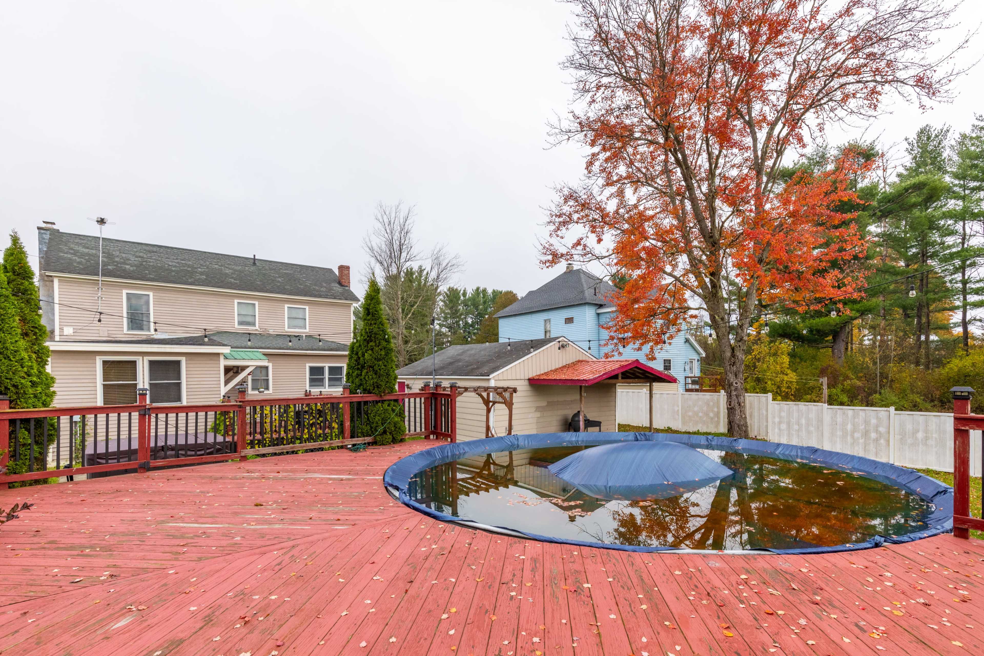The scene shows a backyard deck with a covered pool and nearby houses, surrounded by trees displaying autumn foliage.
