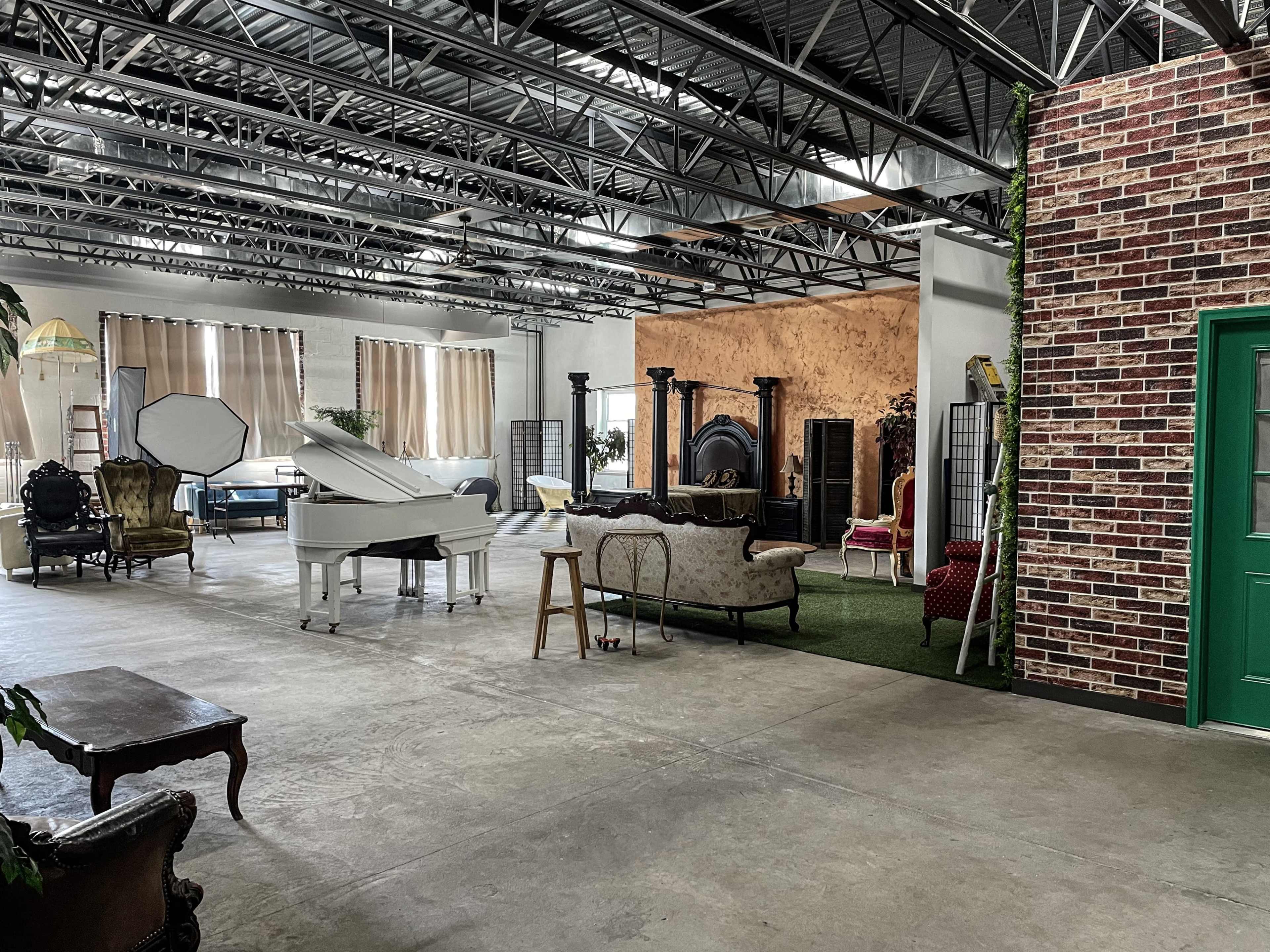 A spacious studio with a grand piano, various seating areas, and decorative elements like plants and a brick wall.