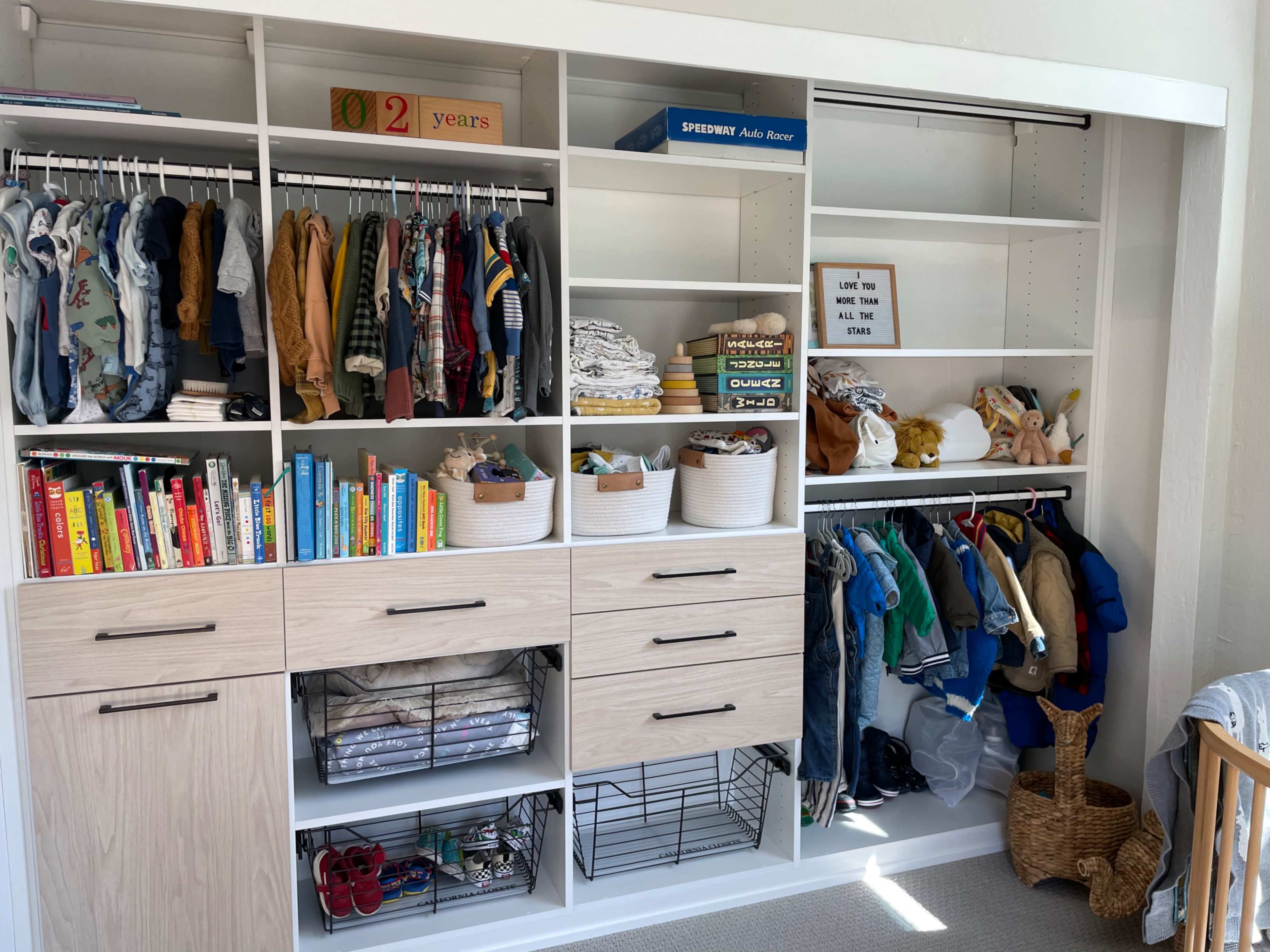 A neatly organized closet with clothes, books, and storage bins arranged on shelves, alongside drawers and an open hanging area for garments.