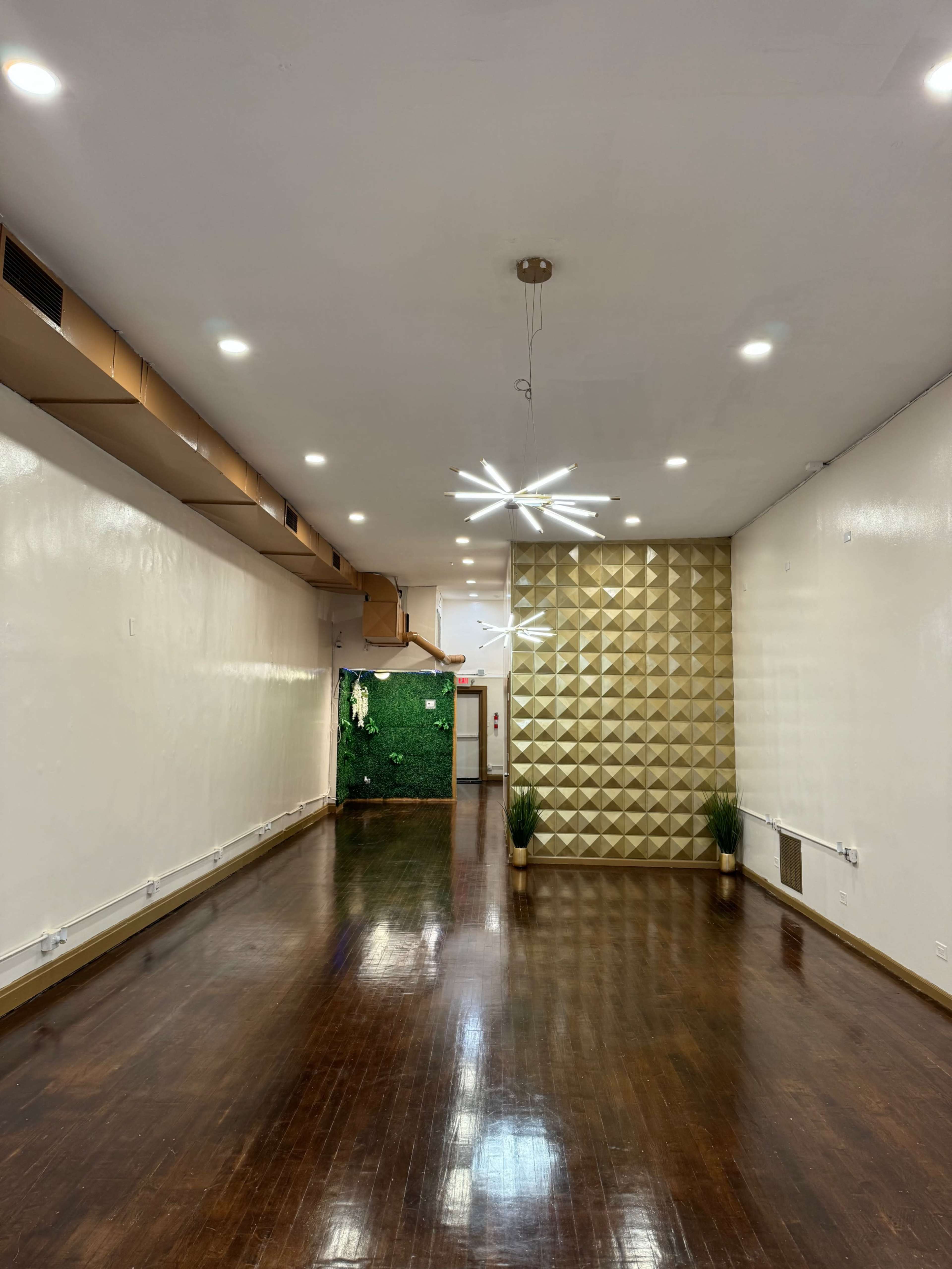 A spacious, well-lit room featuring a textured gold accent wall and dark hardwood flooring.