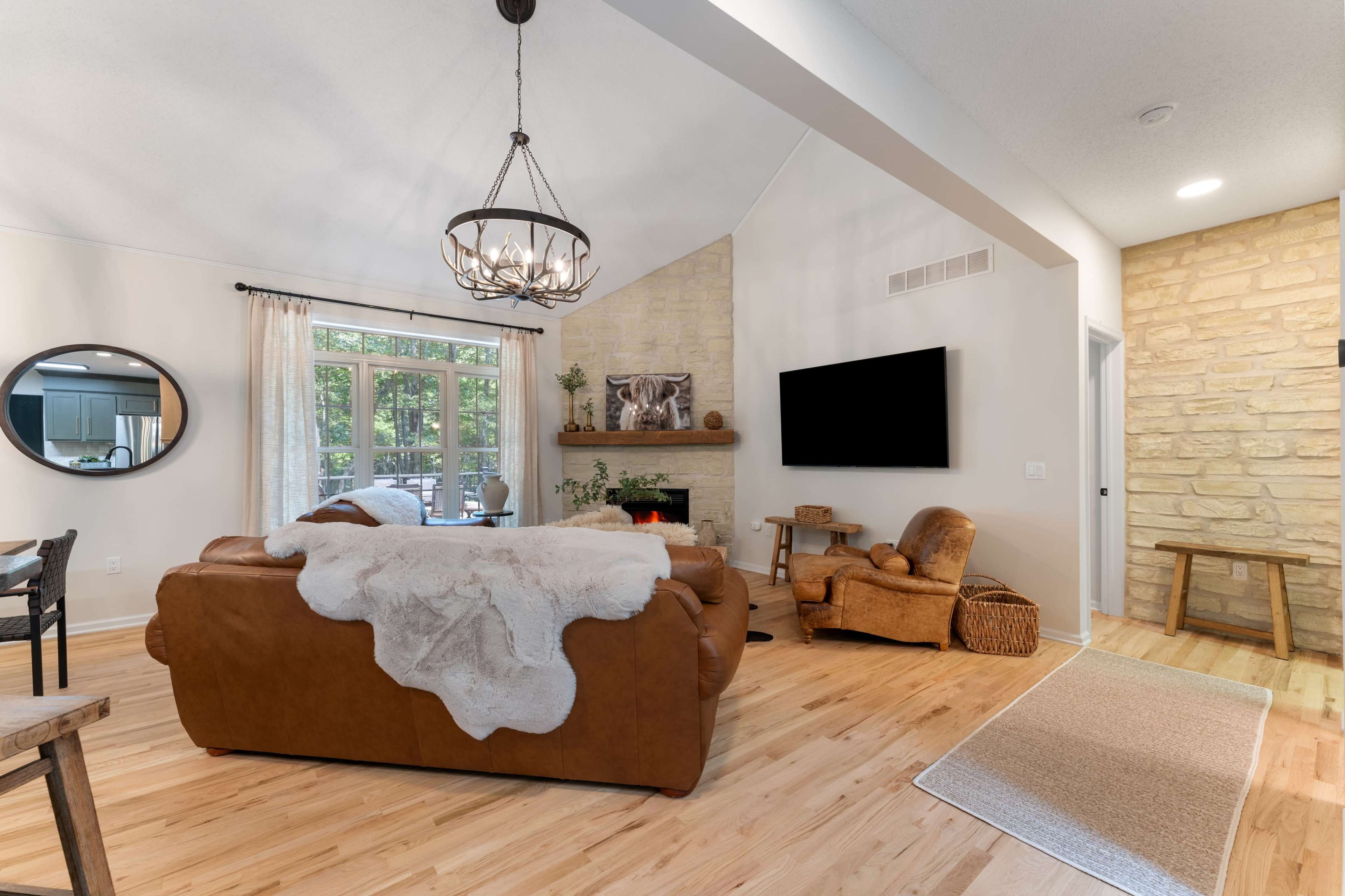 The living room features a leather sofa with a throw blanket, a stone fireplace, and a large flat-screen TV mounted on the wall.