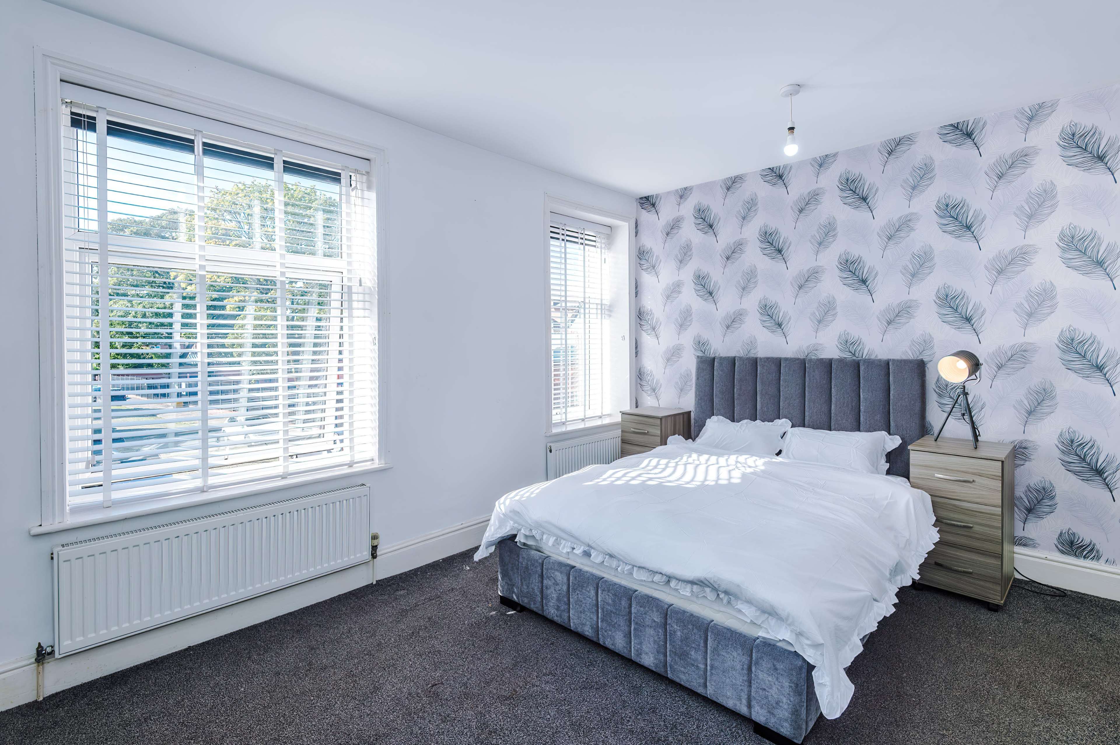 The image shows a bedroom with a bed, two nightstands, and patterned wallpaper featuring leaf designs.