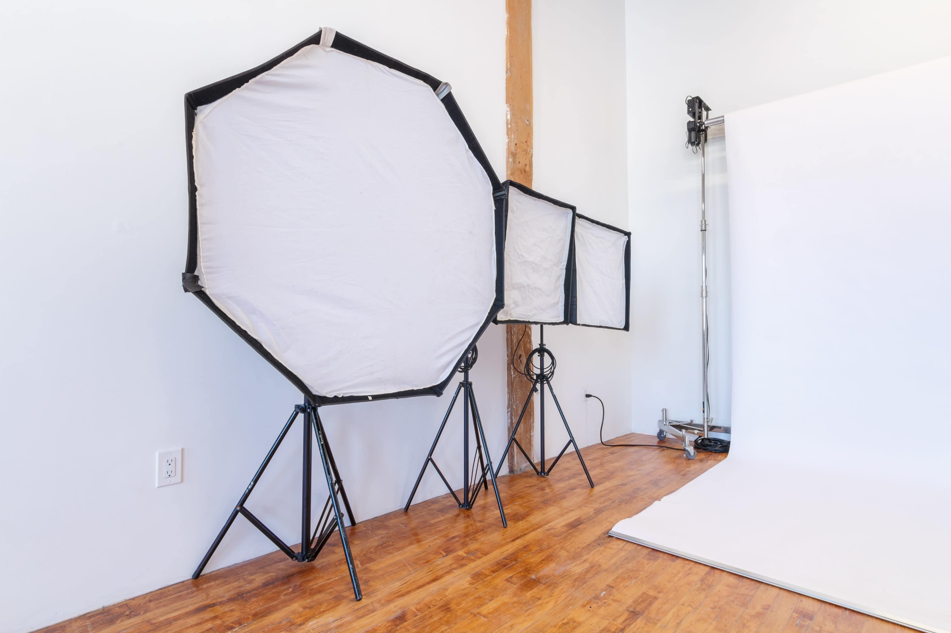 Three softbox lighting setups arranged in a photography studio with a smooth, white backdrop and wooden flooring.