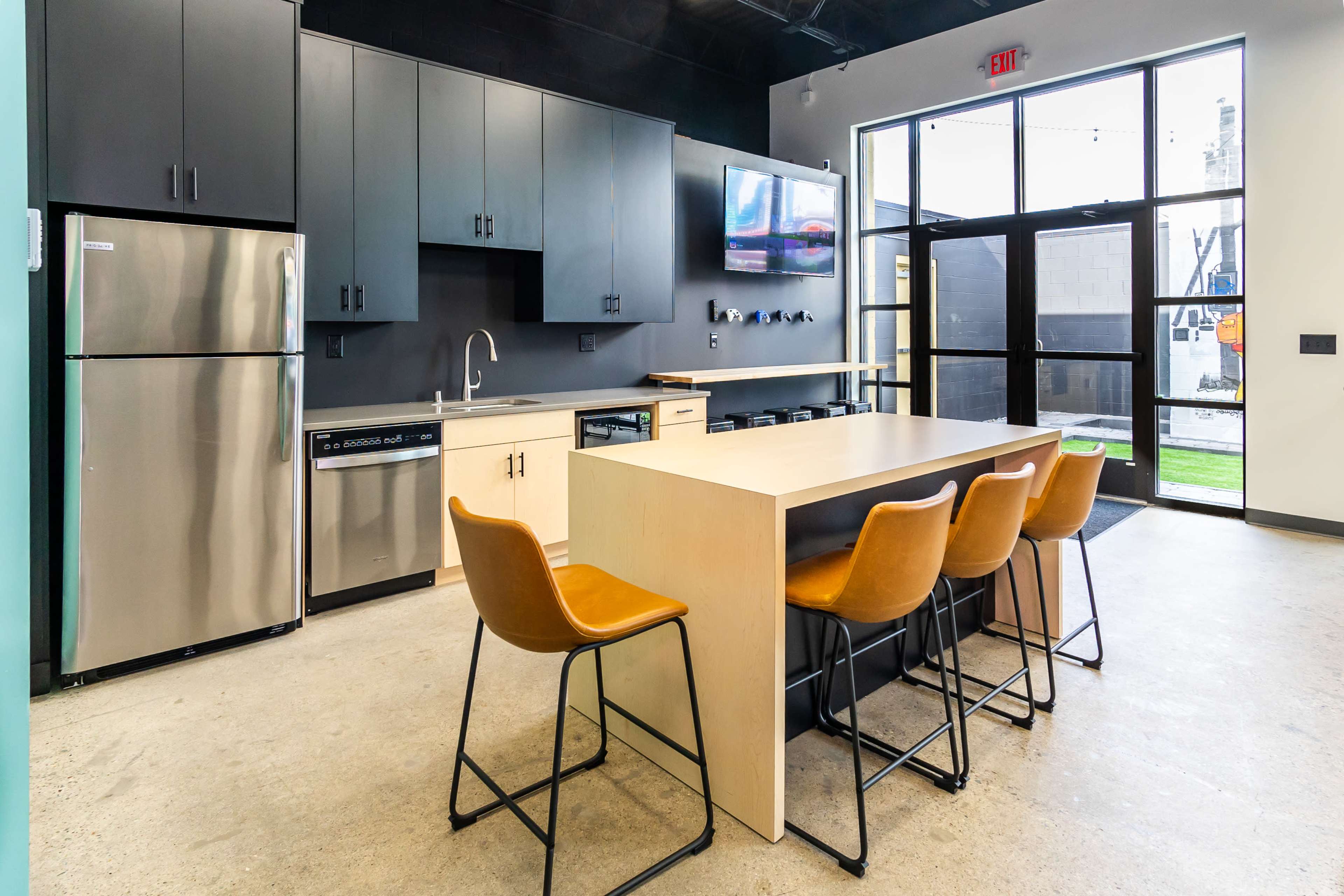 The image shows a modern kitchen with stainless steel appliances, a large island with bar seating, and a glass door leading to an outdoor area.