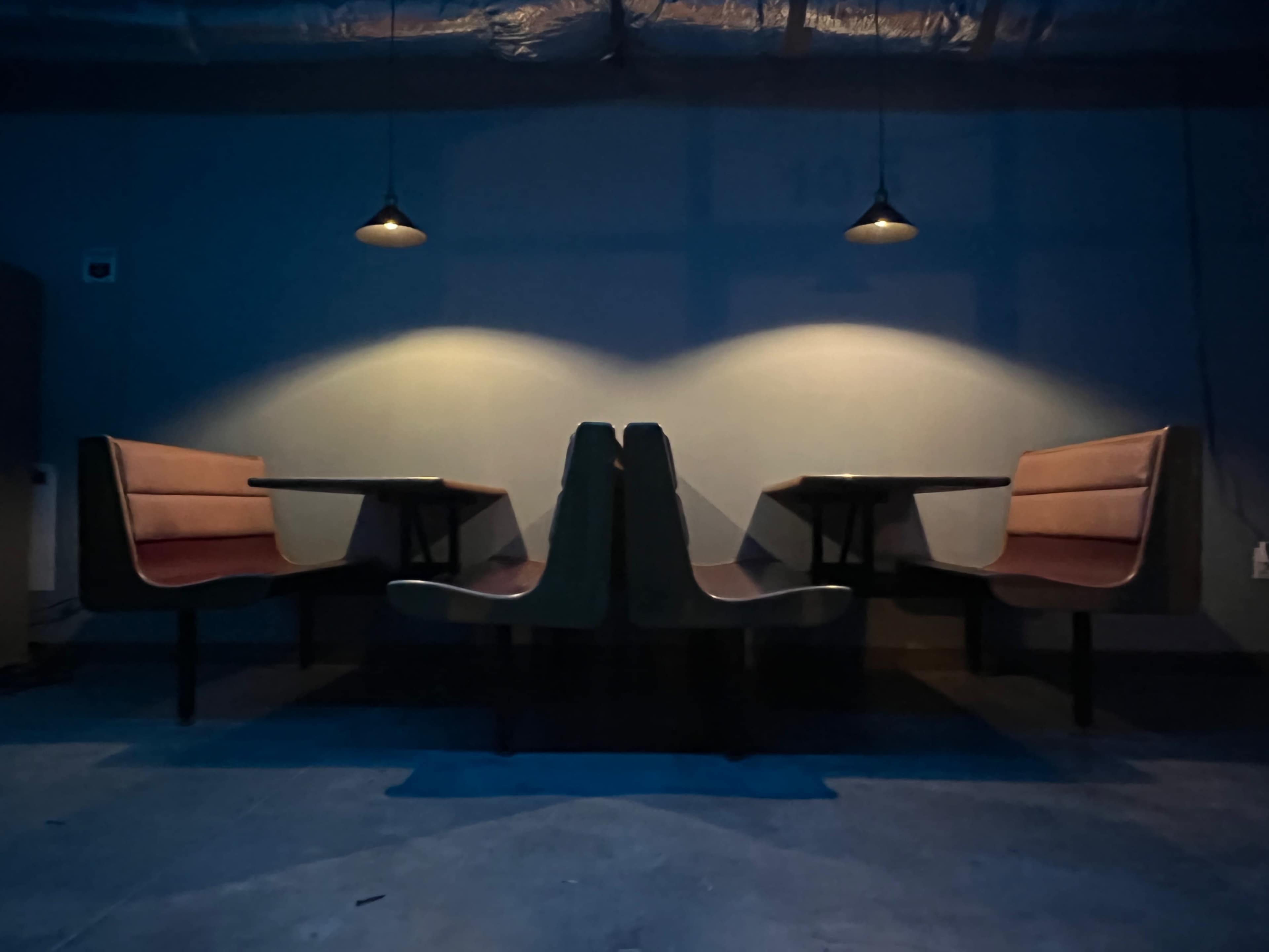 The image shows a dimly lit café interior with two long booths facing each other, illuminated by overhead pendant lights.