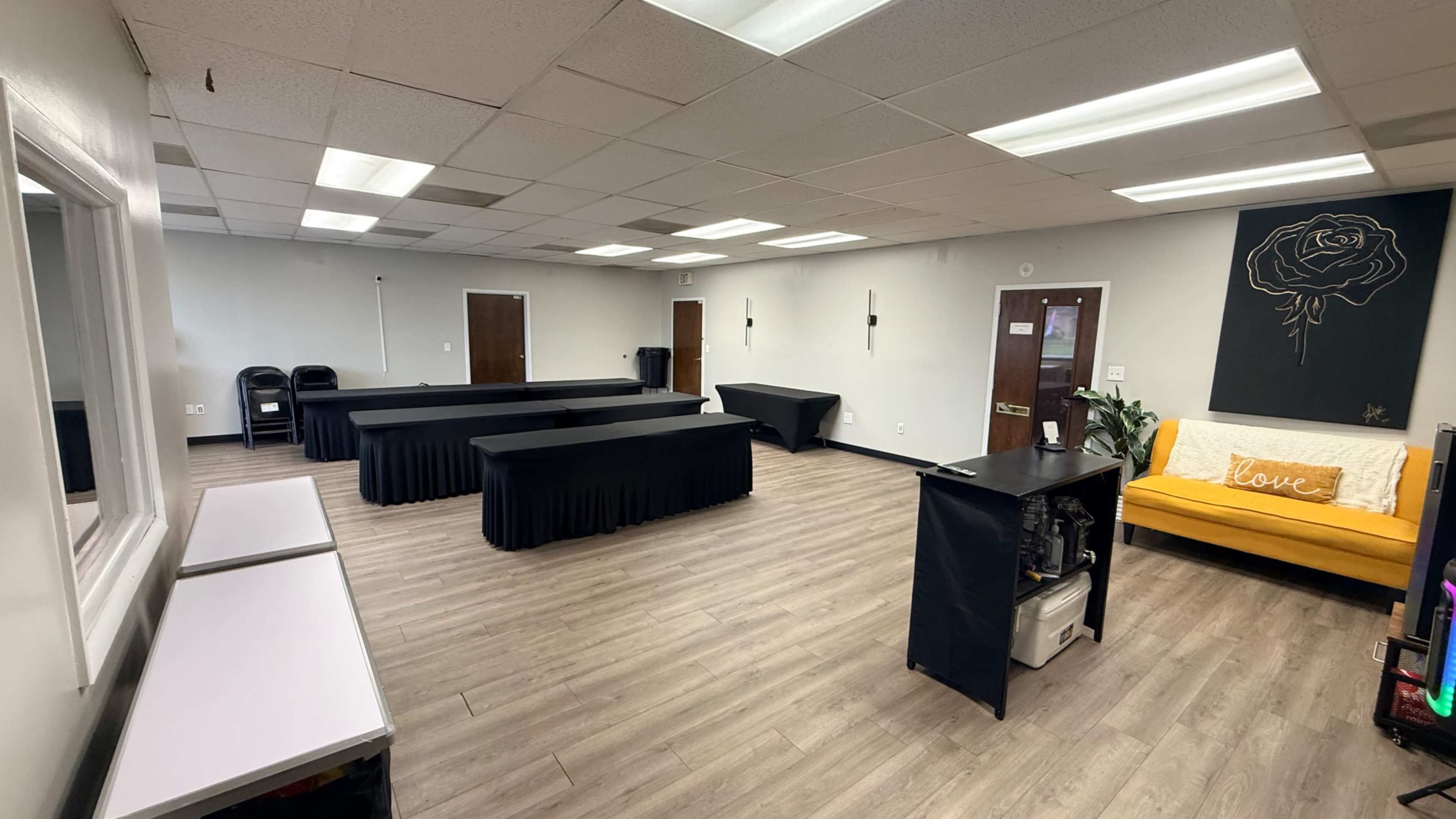The room features a yellow couch, several black tables arranged throughout, and a mirrored wall.