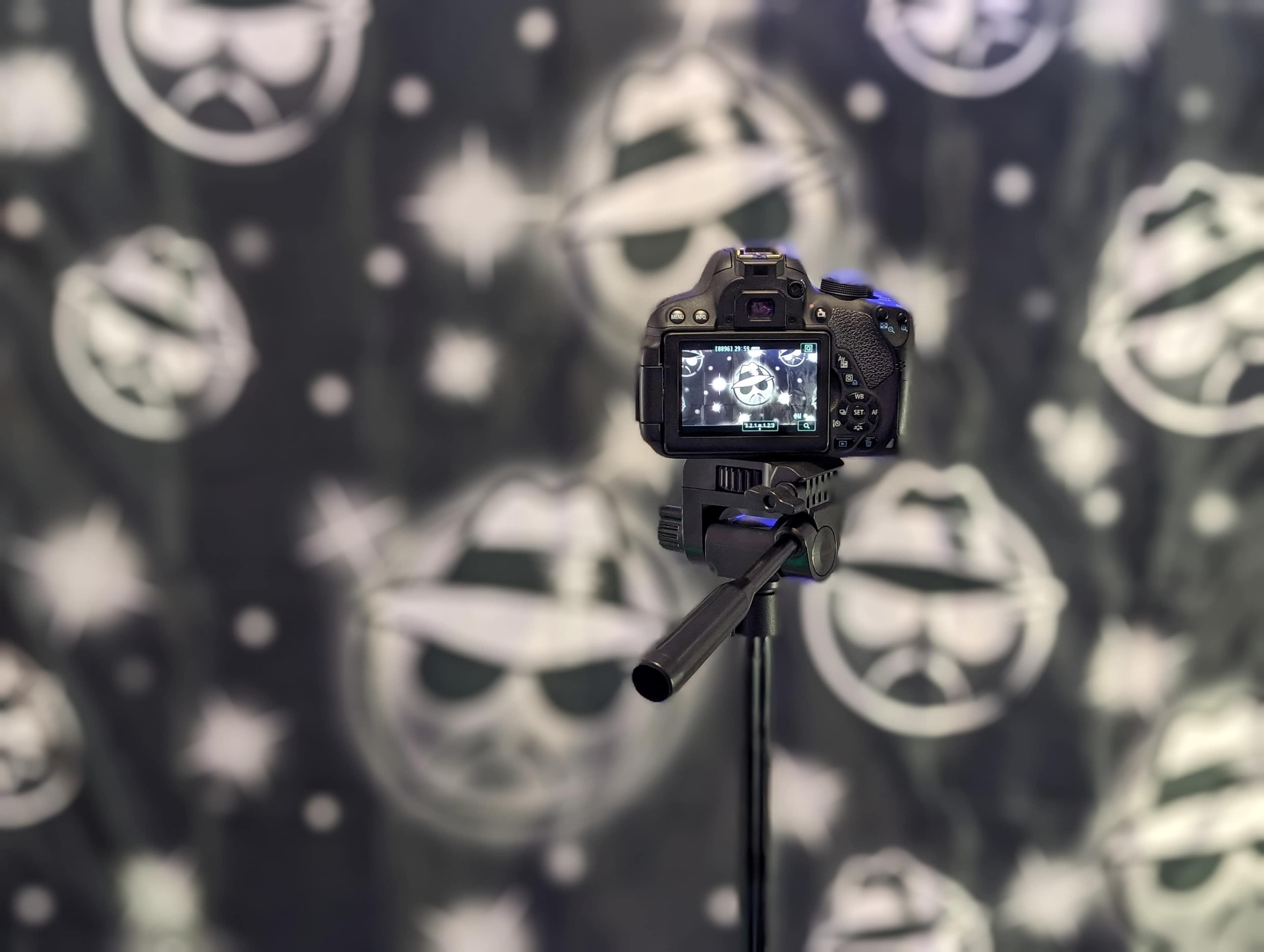 A camera on a tripod is focused on a backdrop with graphic designs of sunglasses and peace signs.