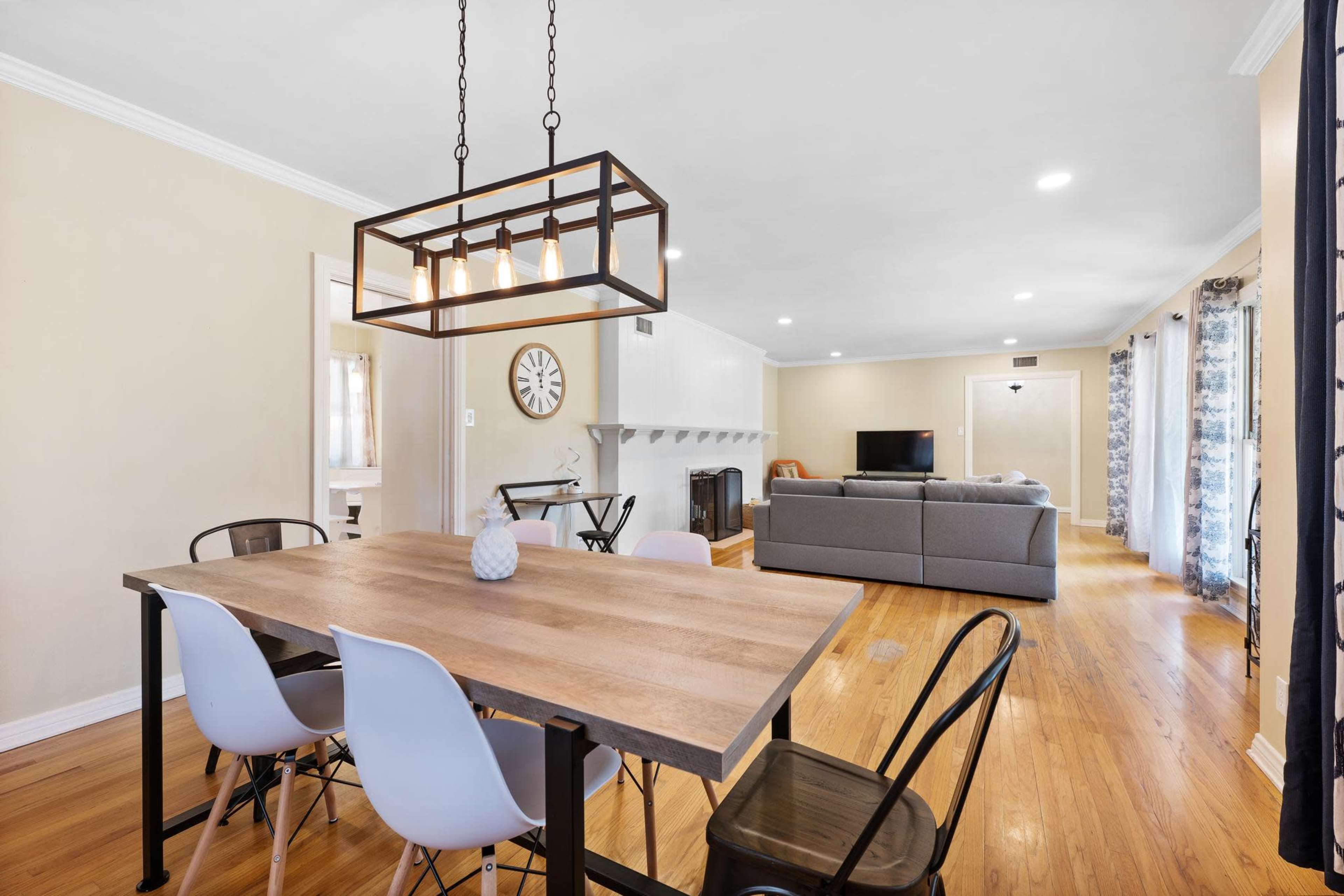 A spacious dining area features a wooden table with modern chairs, leading into a well-lit living room with a gray sofa and television.