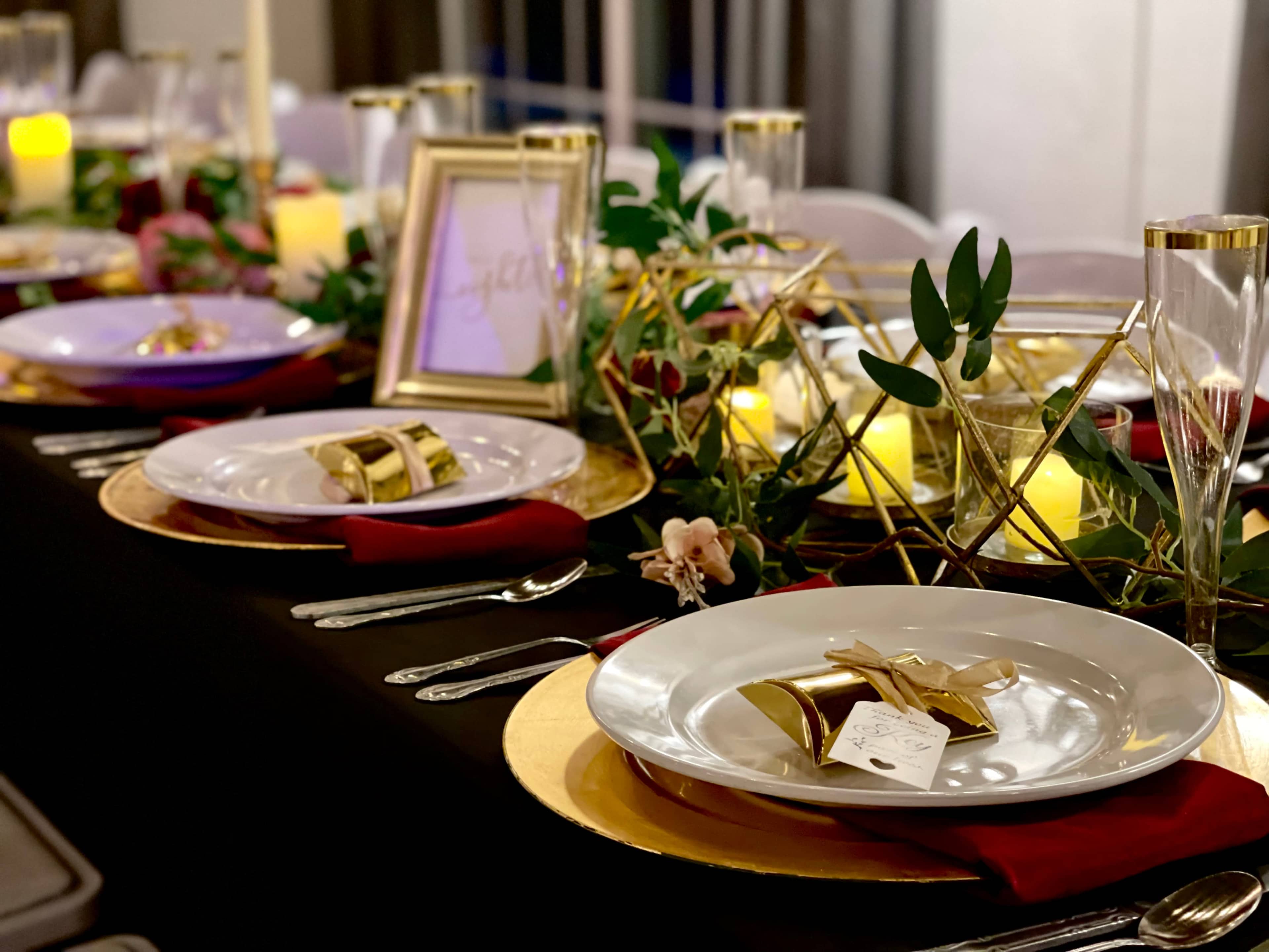 A beautifully arranged dining table features elegant plates, decorative gold accents, and lush greenery, creating an inviting atmosphere for a gathering.
