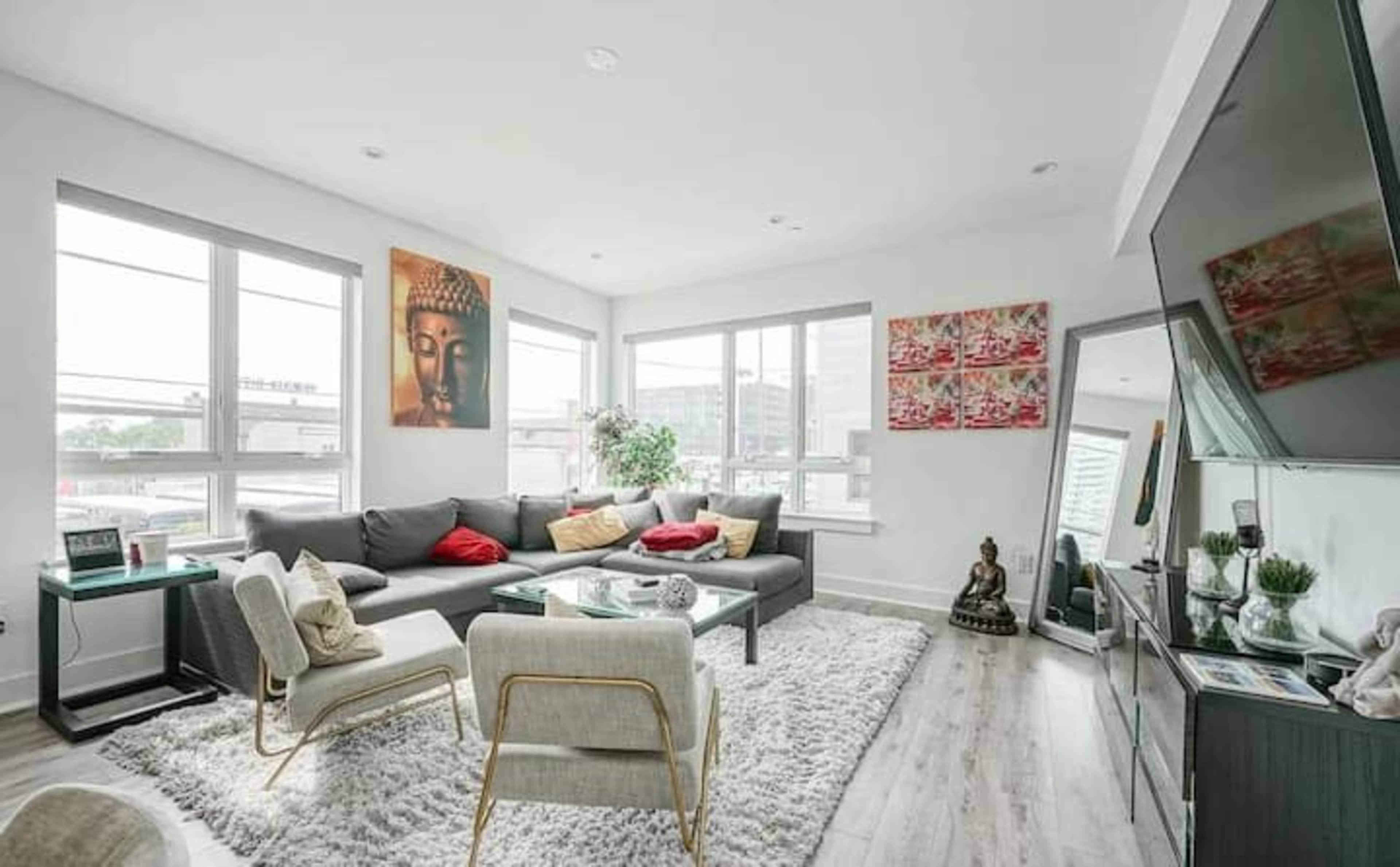 The living room features a gray sectional sofa with red cushions, a glass coffee table, and decorative artwork on the walls, including a Buddha image and a statue.