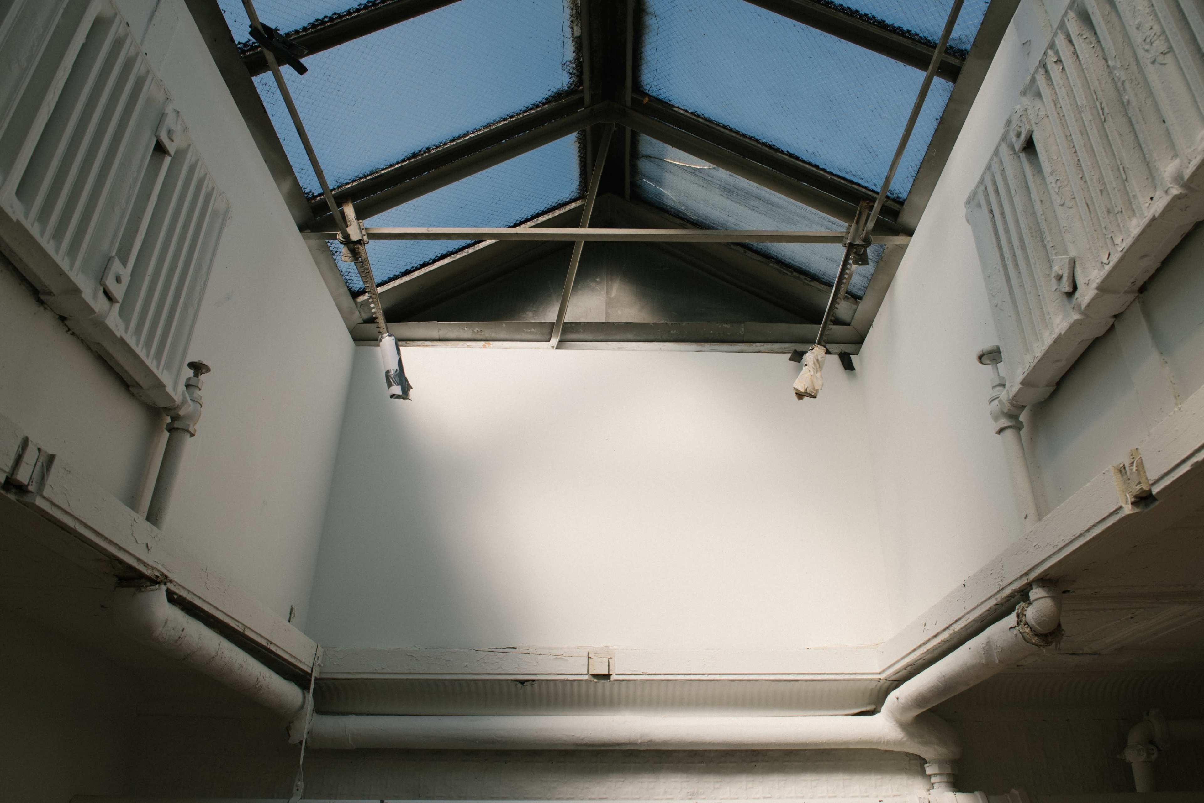 An interior space with a skylight, revealing a ceiling and walls that are lightly colored, along with exposed pipes and radiators.