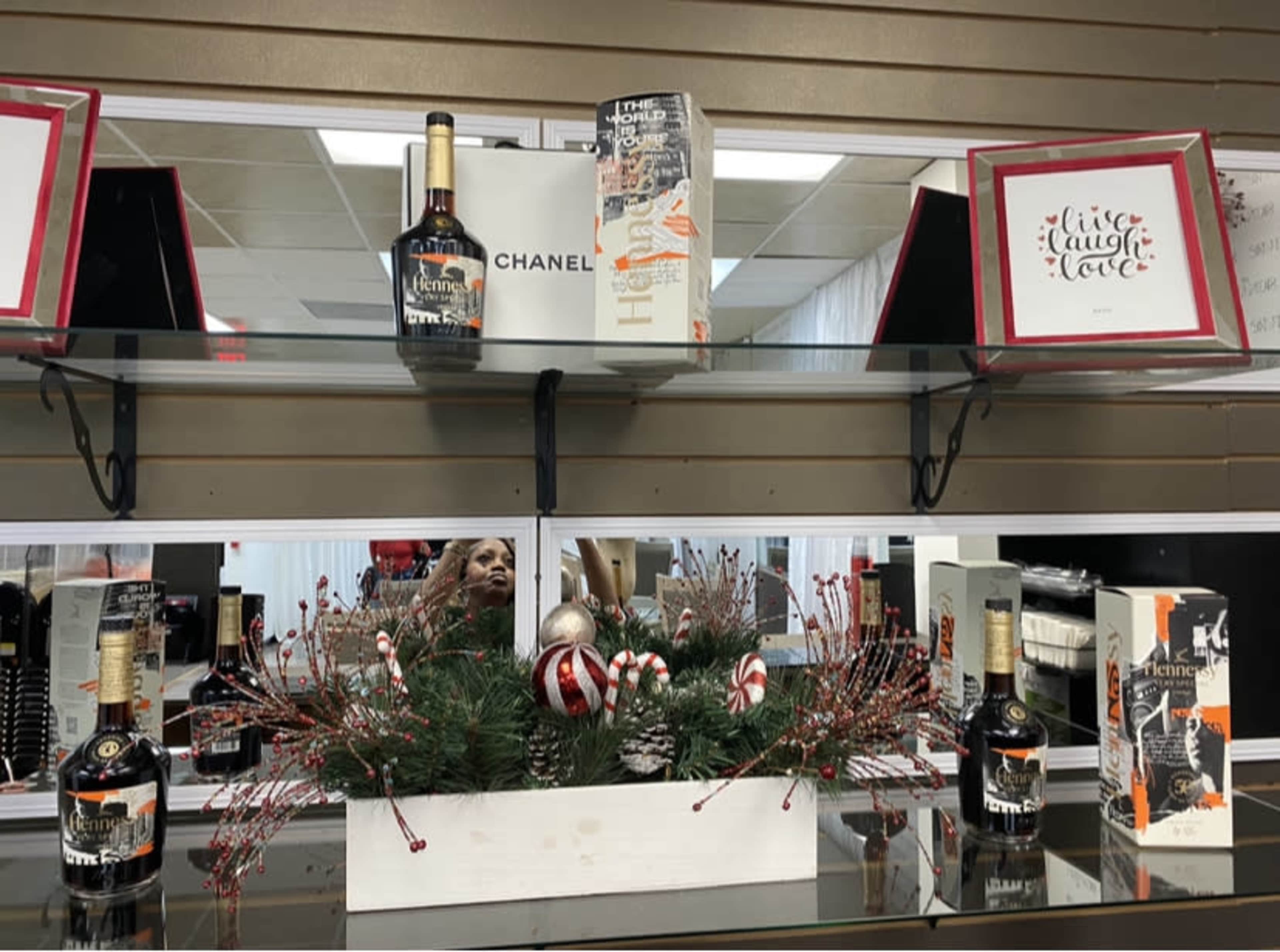 The image shows a shelf display featuring various bottles of liquor, including a prominent bottle of Hennessy, alongside decorative items such as a Chanel box and a seasonal arrangement with red and white ornaments.