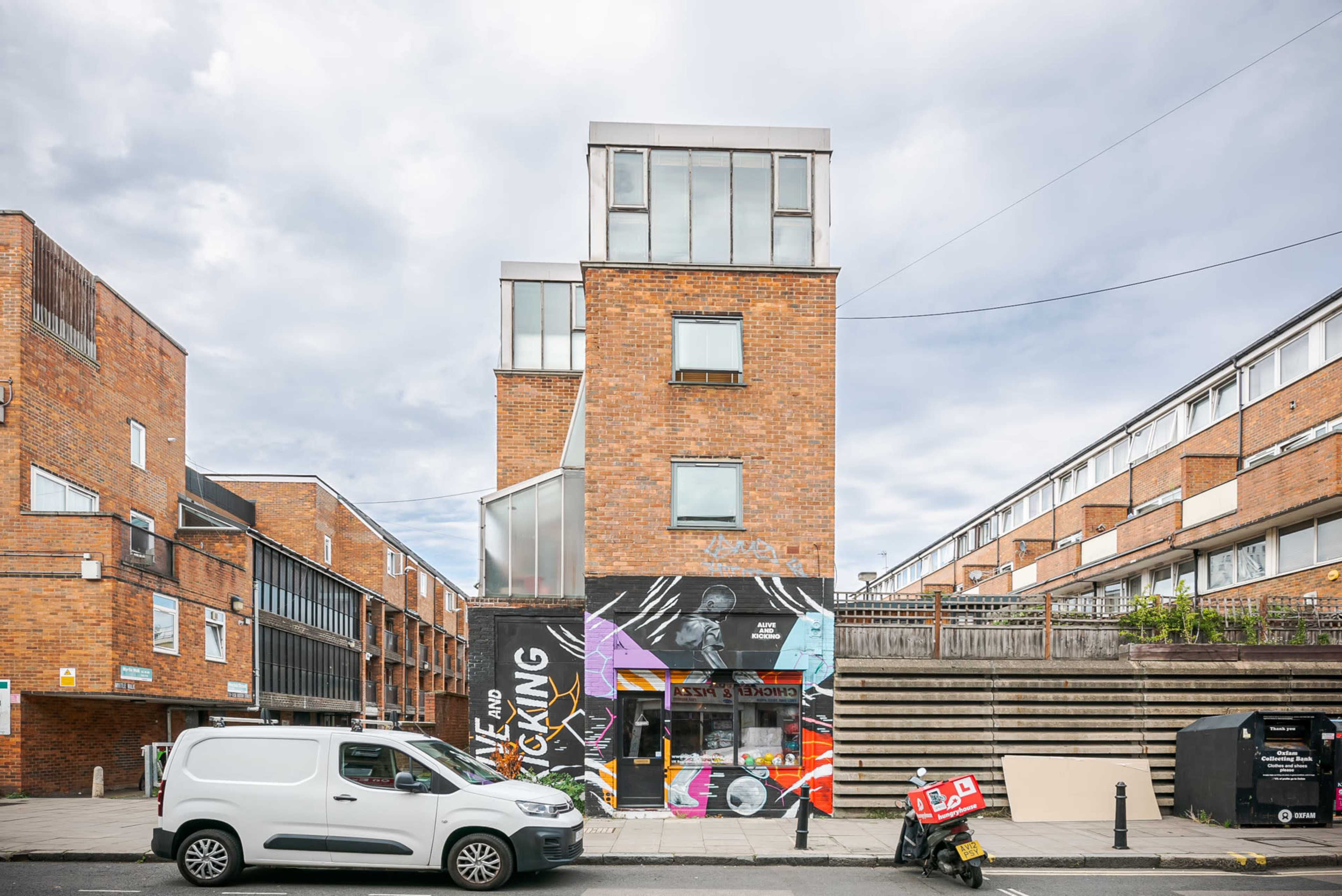 A brick building with a modern top section, featuring a large mural on the front and a white van parked in front.
