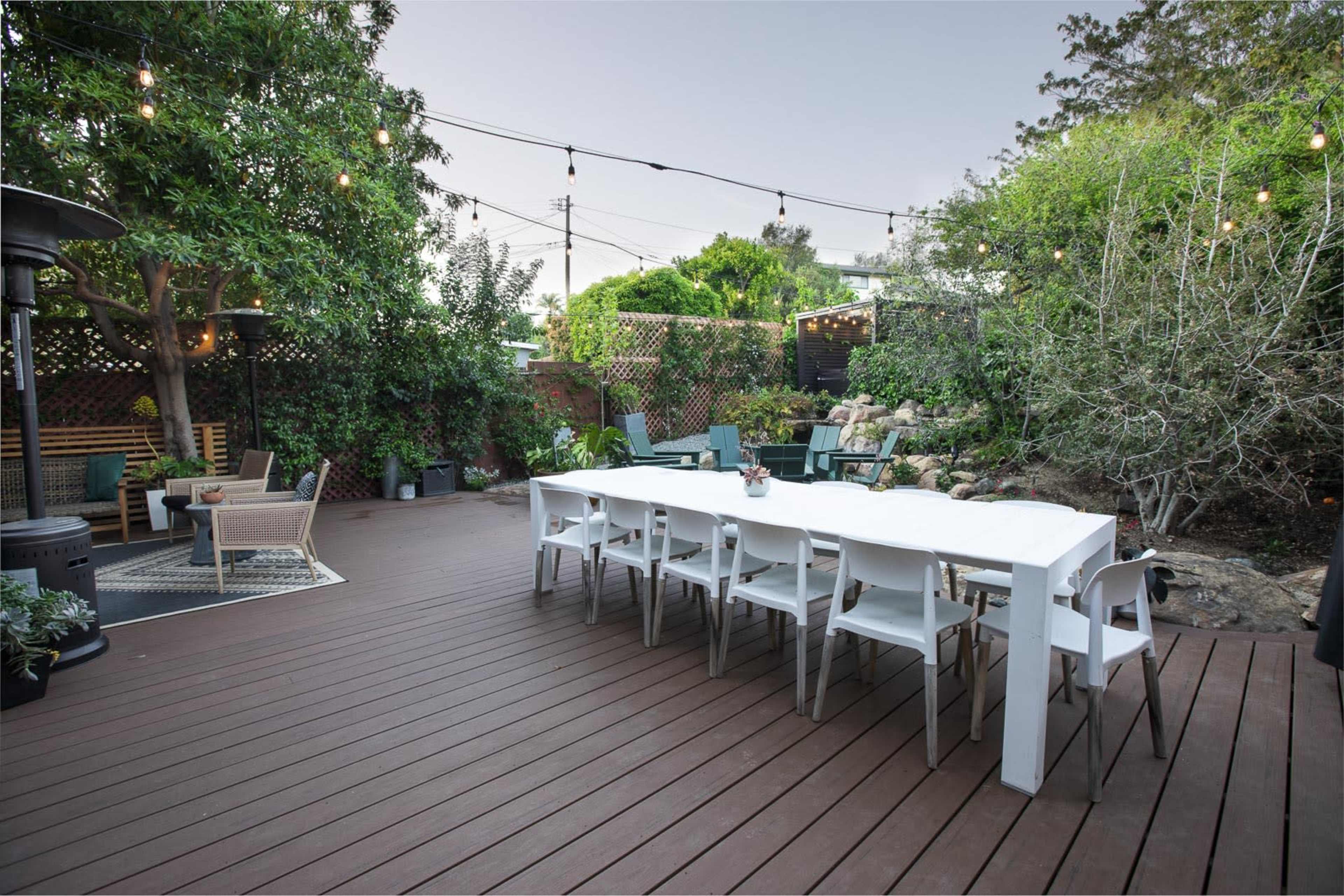 A spacious outdoor patio with a long white dining table, surrounded by chairs, and adorned with string lights and greenery.