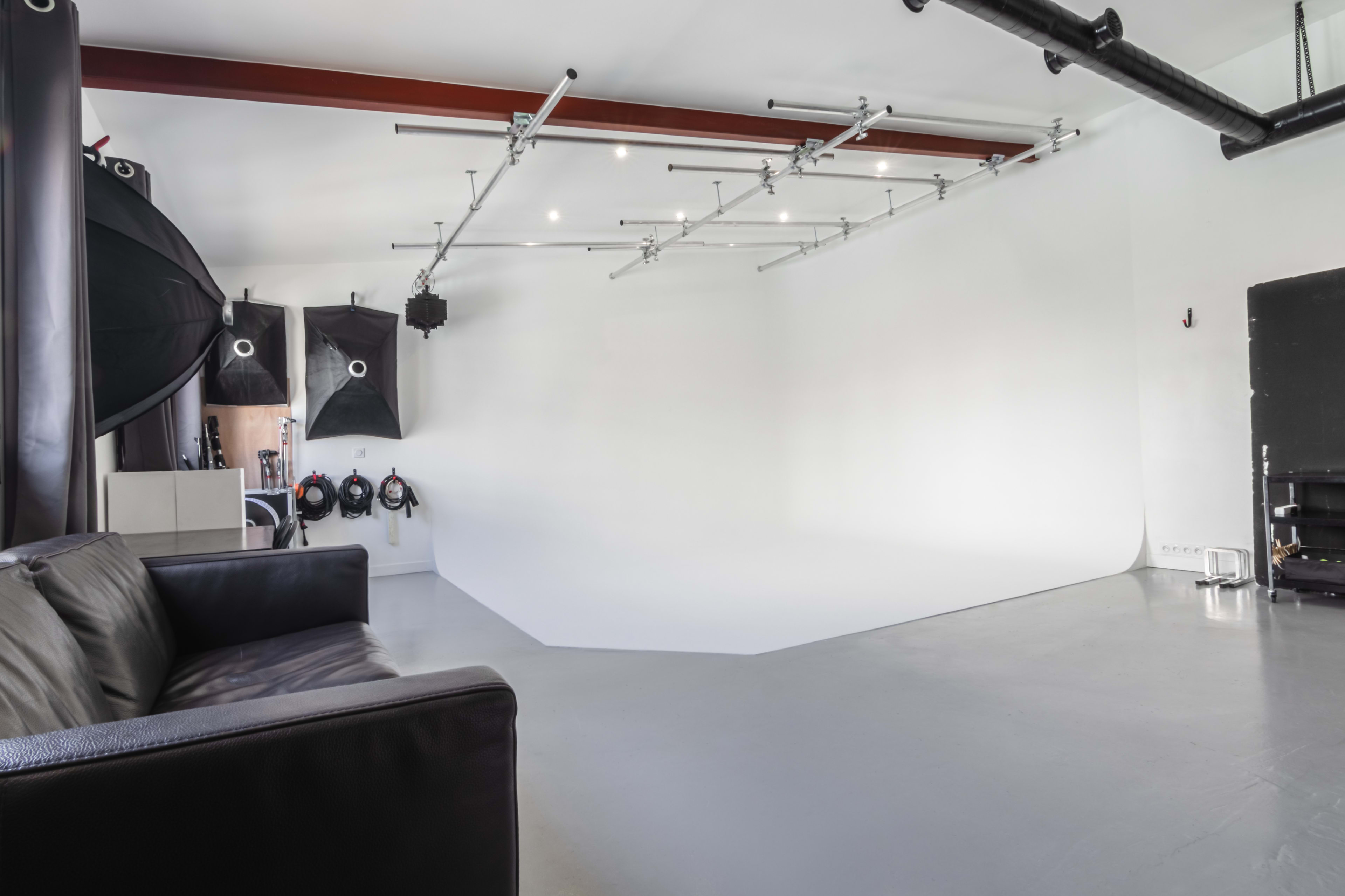 A photography studio with a seamless white backdrop, professional lighting equipment, and a black sofa in the foreground.