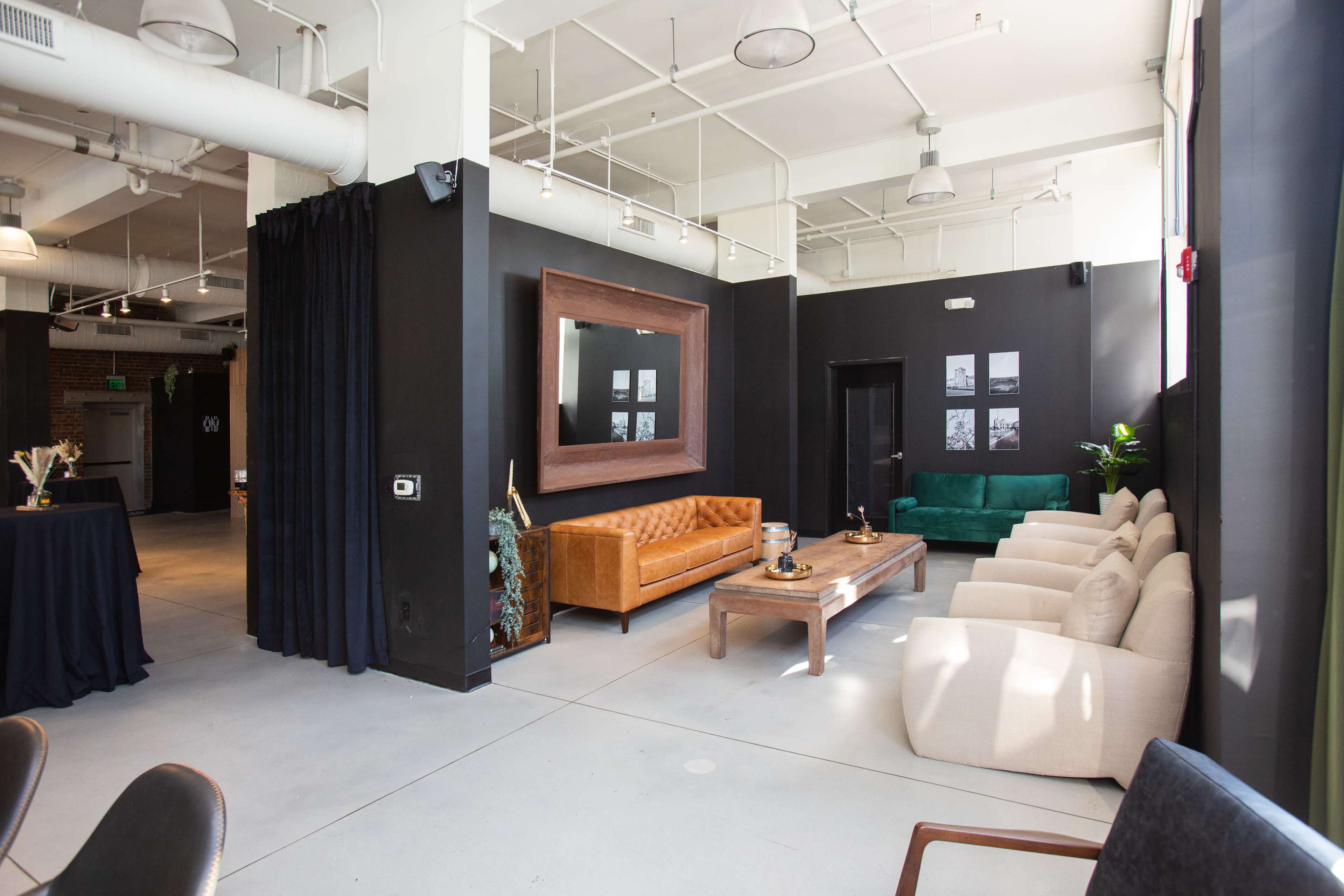 The image shows a modern interior space featuring a combination of seating areas, including a brown leather couch, a green couch, and beige armchairs, along with a large mirror and framed pictures on the walls.