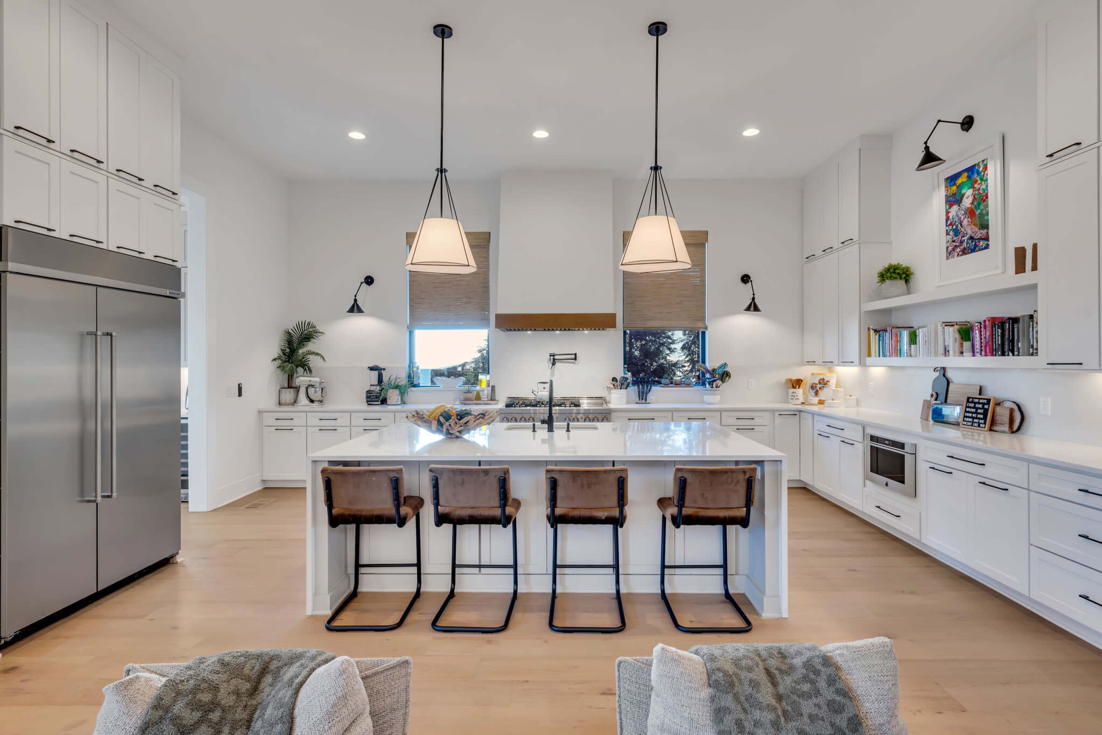A modern kitchen features a central island with bar stools, stainless steel appliances, and ample cabinet space under bright lighting.