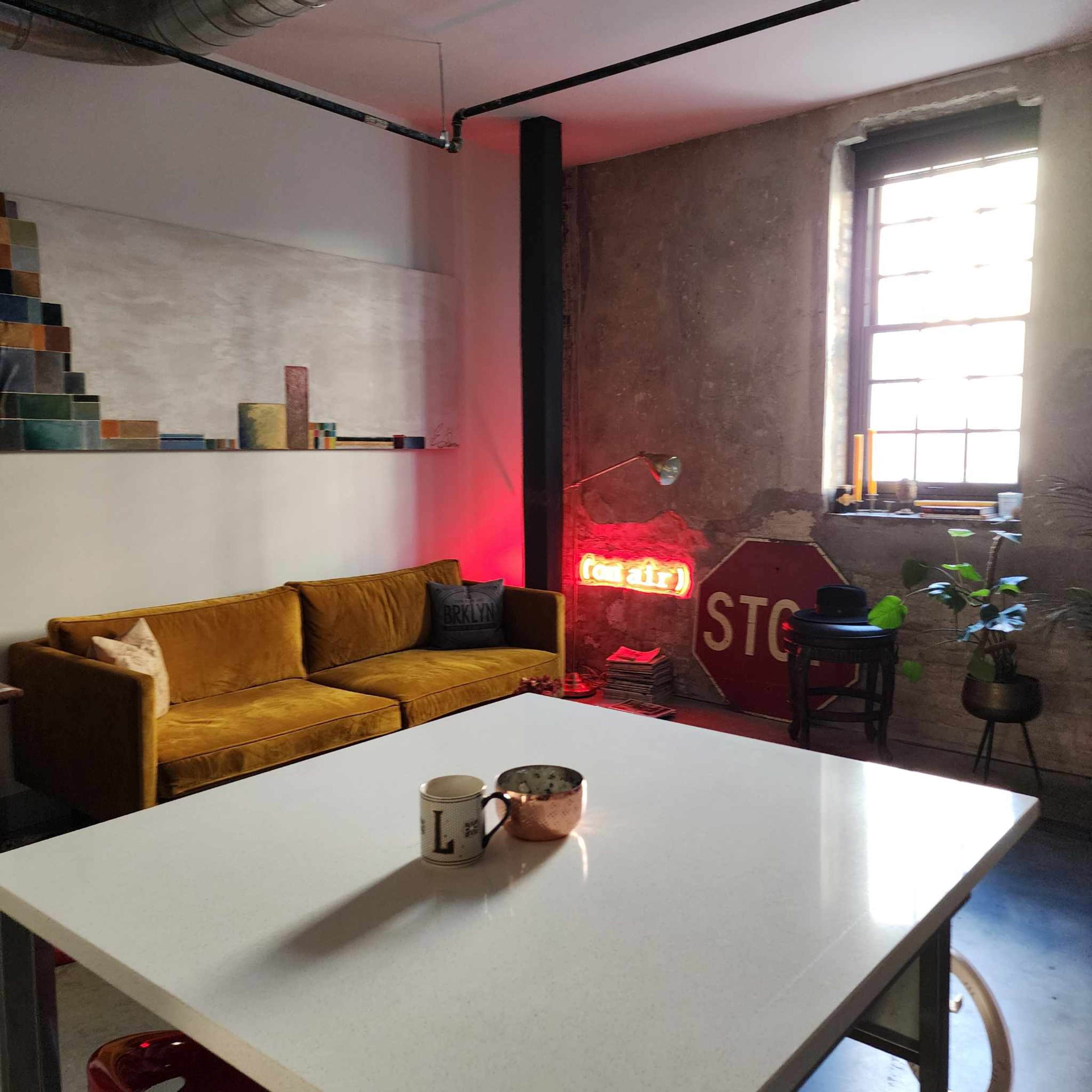 A modern interior space featuring a yellow sofa, a white table, a neon "STOP" sign, and a large window letting in light.
