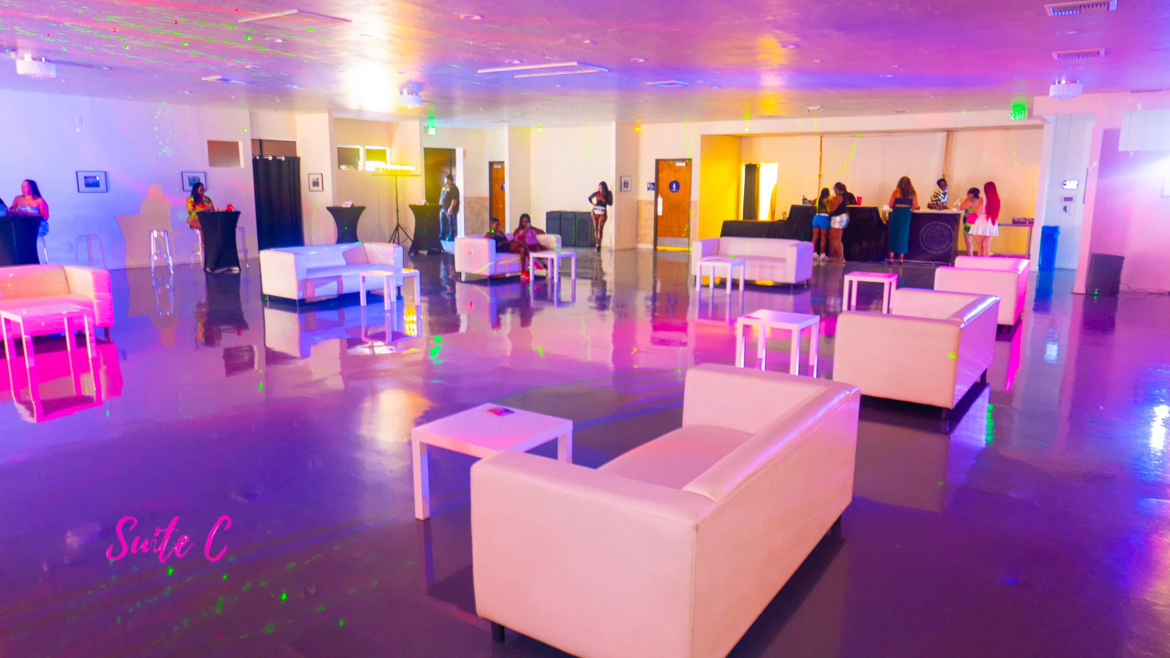 A spacious event hall with white furniture, including sofas and tables, and colorful lights reflected on the floor.