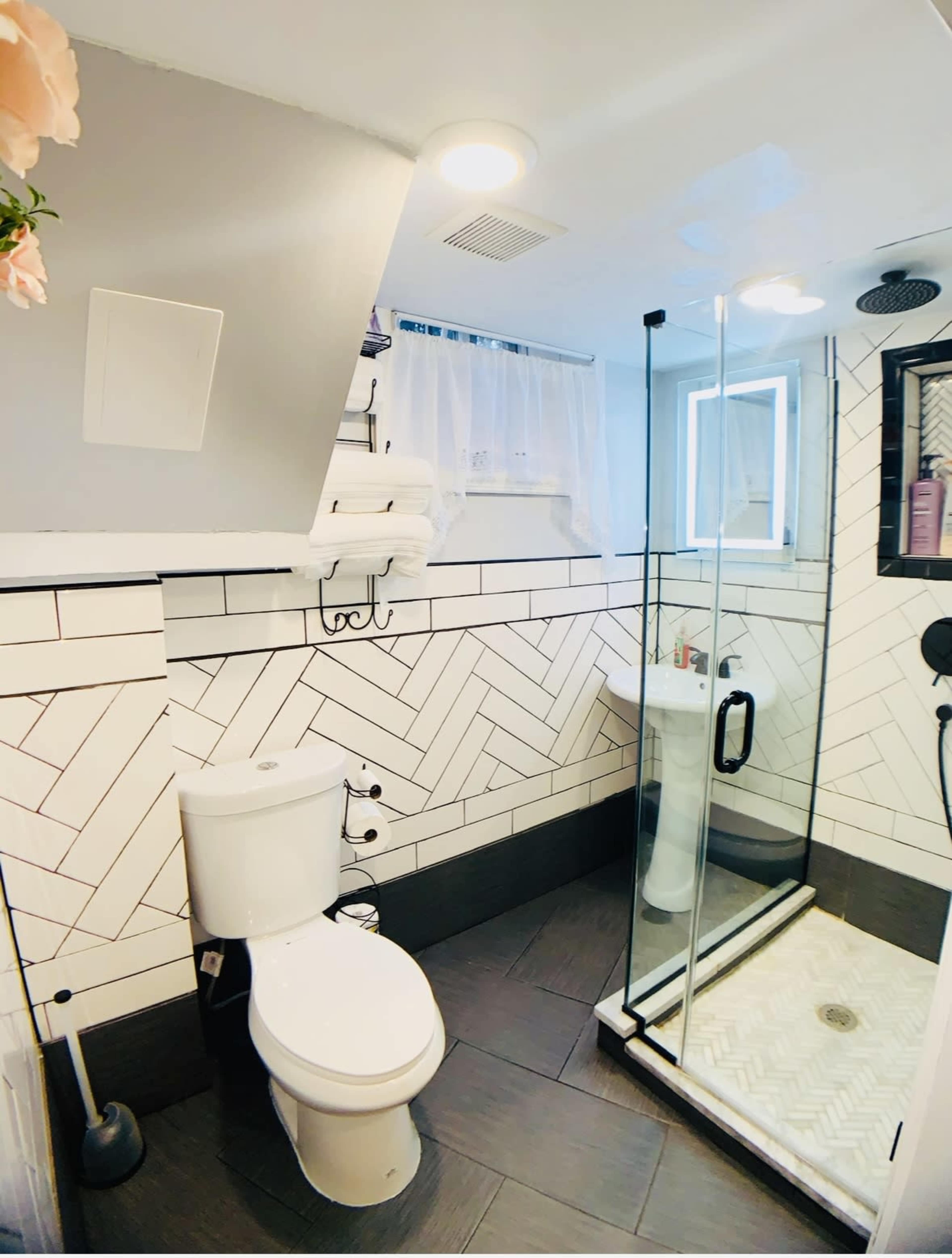 A modern bathroom featuring a glass shower stall, a toilet, and a herringbone-patterned tile wall.