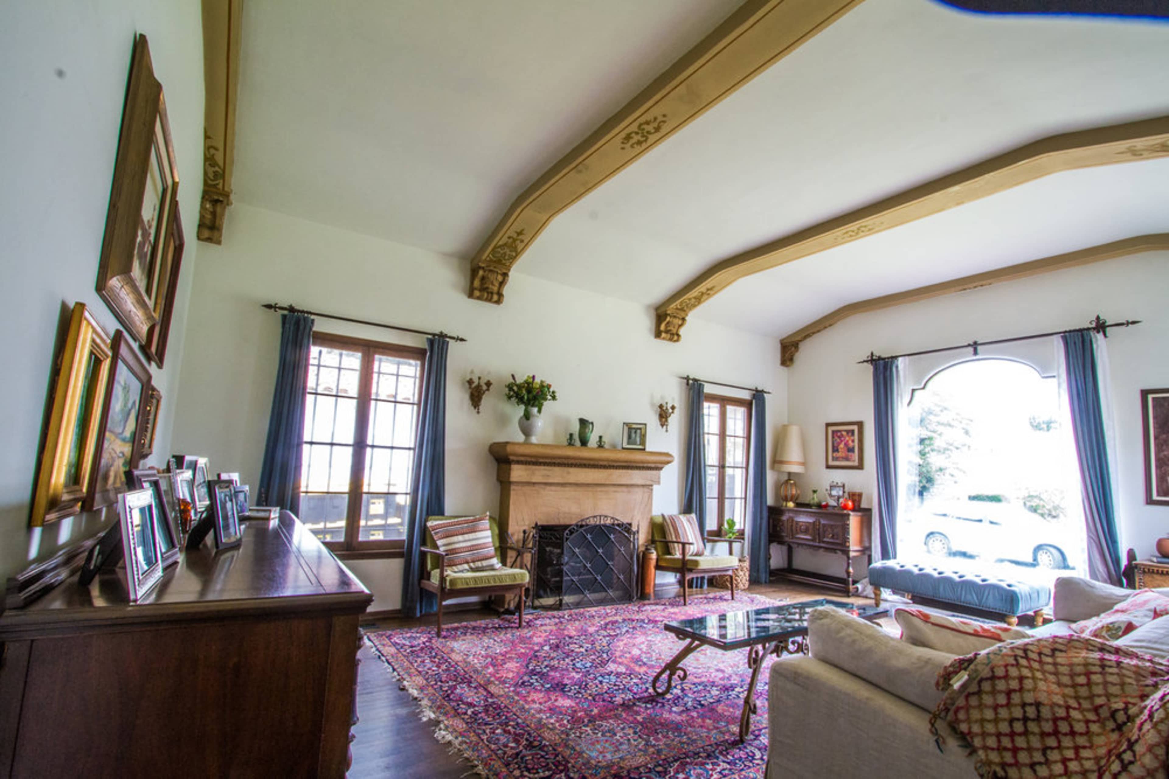 A spacious living room featuring a fireplace, large windows, a patterned rug, and various framed photographs on display.