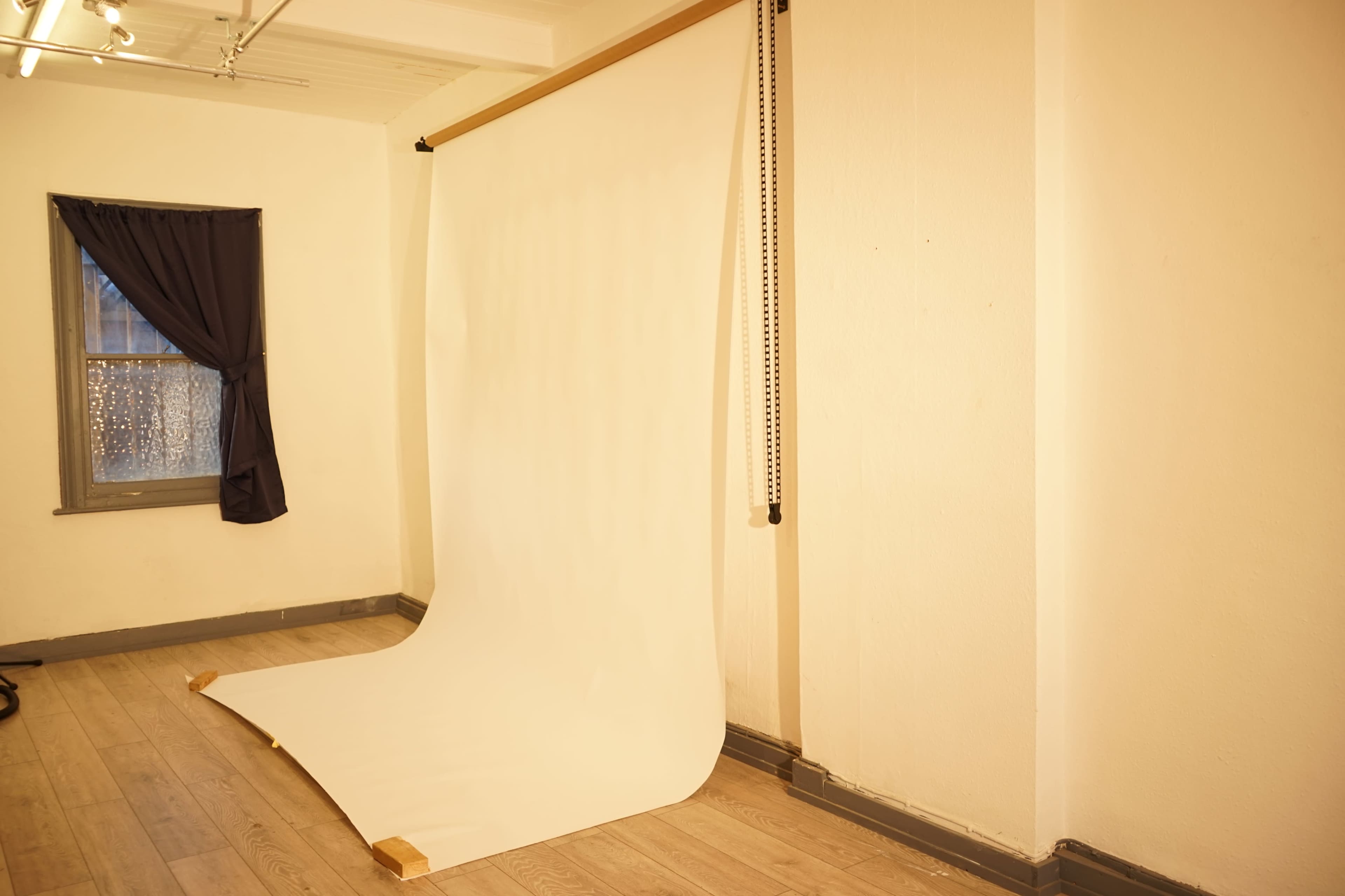 The image shows a blank white backdrop set up in a well-lit room with a window and a dark curtain.