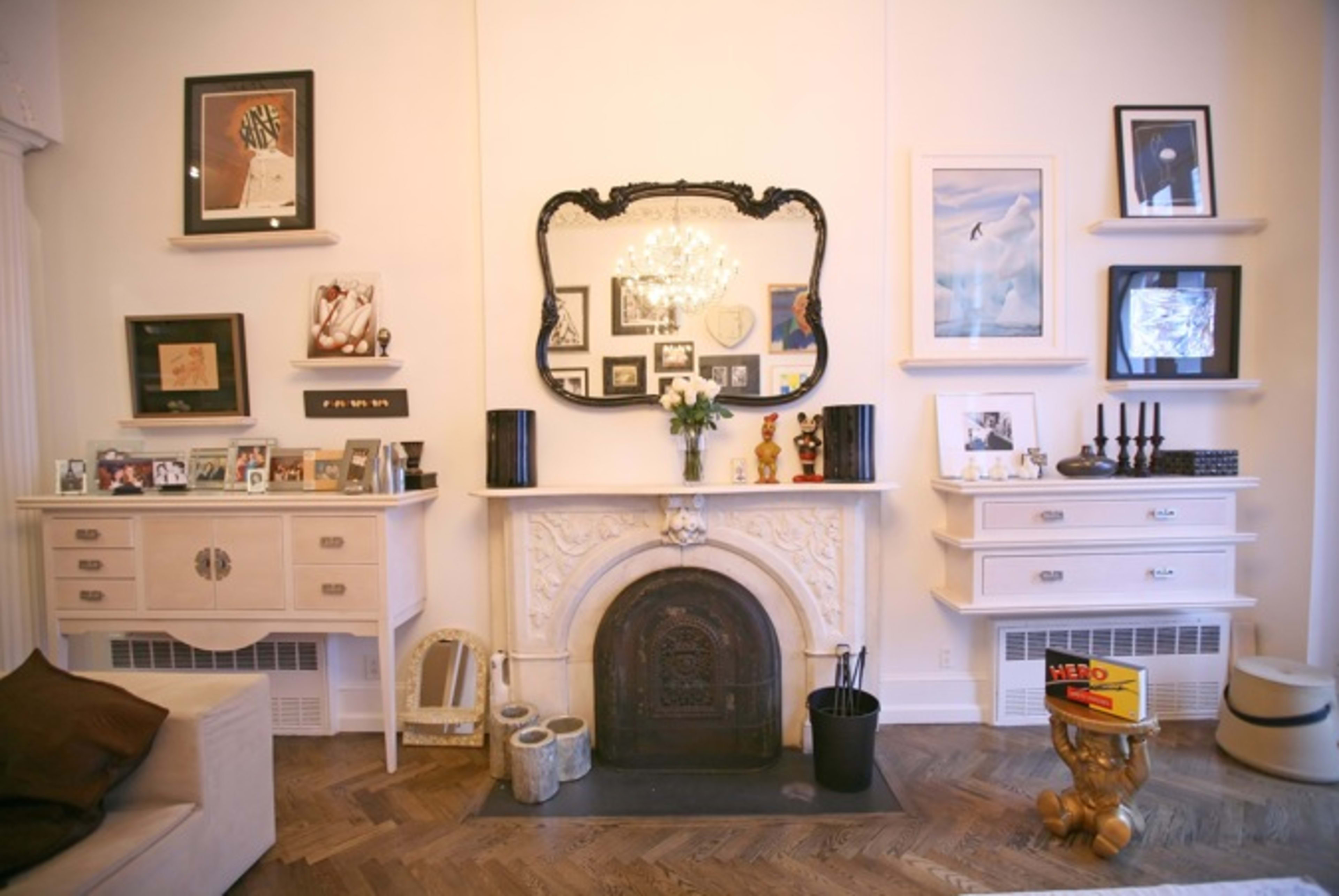 The image shows a living room with a decorative fireplace at the center, flanked by framed artwork and photographs on the walls.
