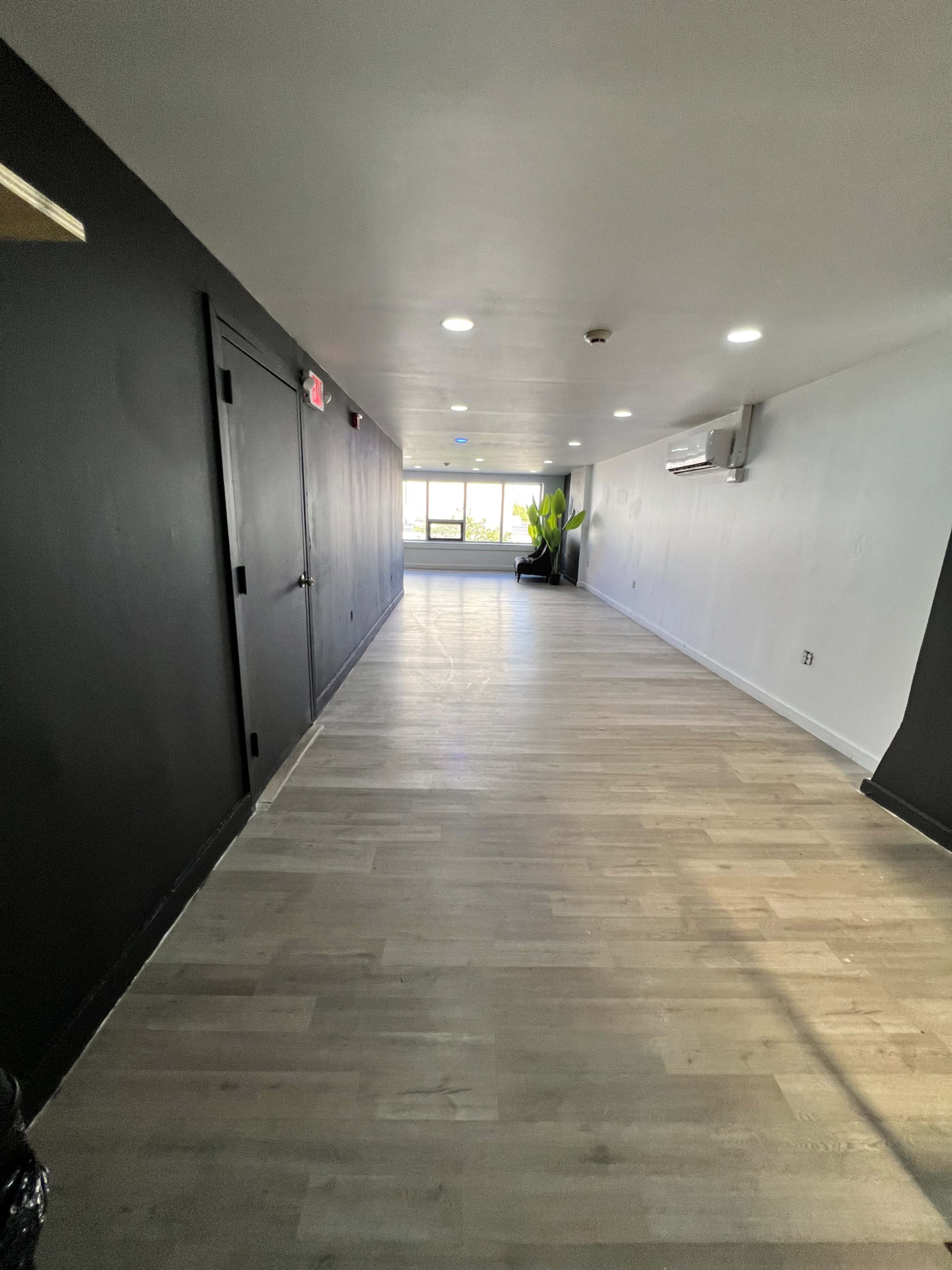 A long, empty hallway with a smooth wooden floor and windows at the far end.